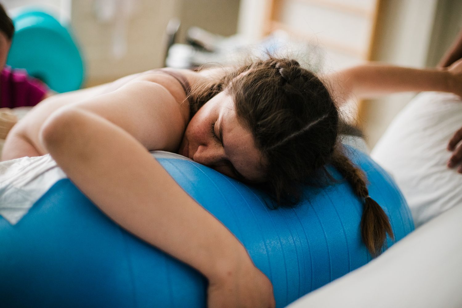 Woman in active labor leans over blue birthing ball for natural pain management during home birth.