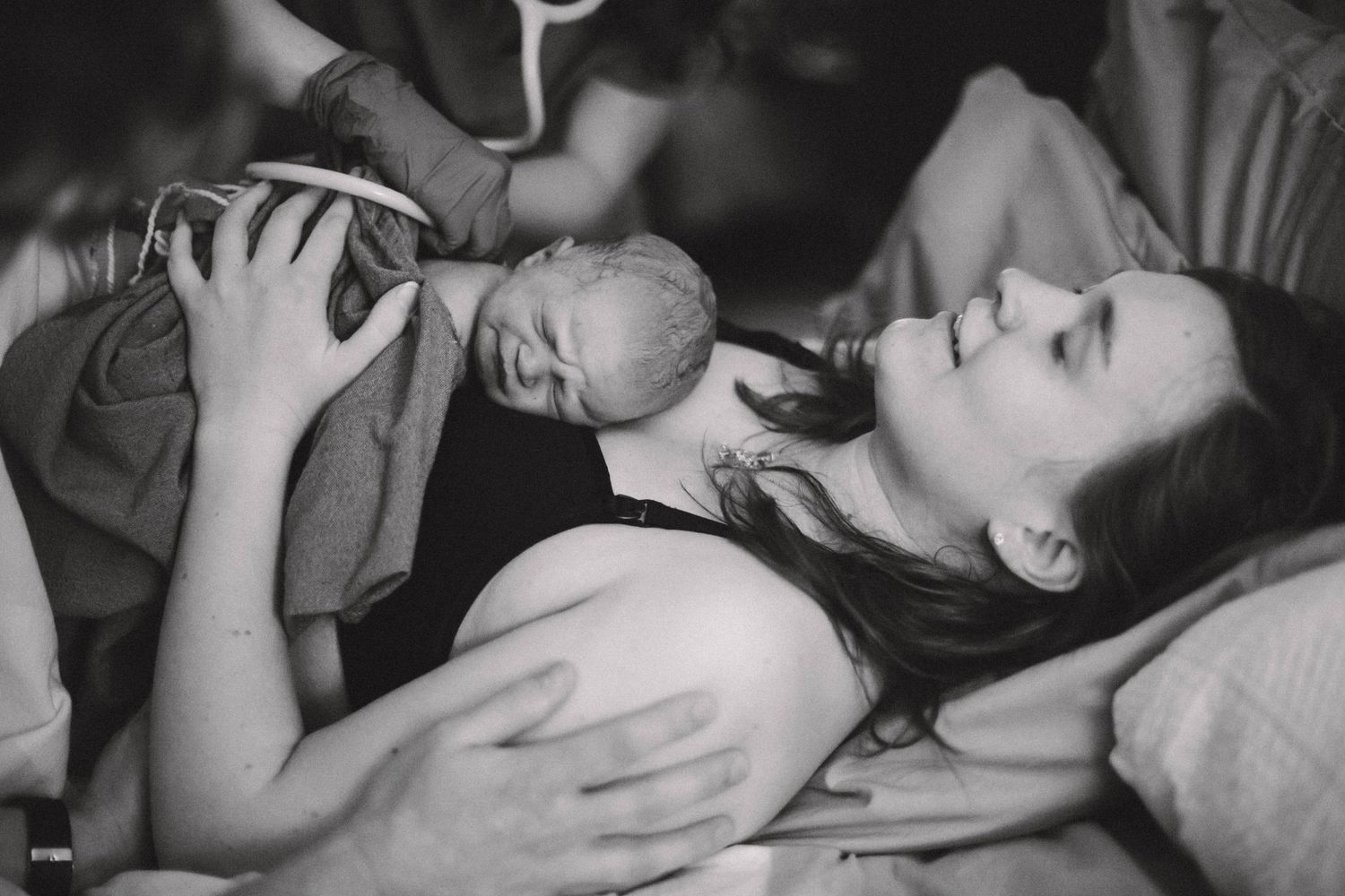 Black and white photo of a mother lying in bed, smiling as she holds her newborn baby for the first time.