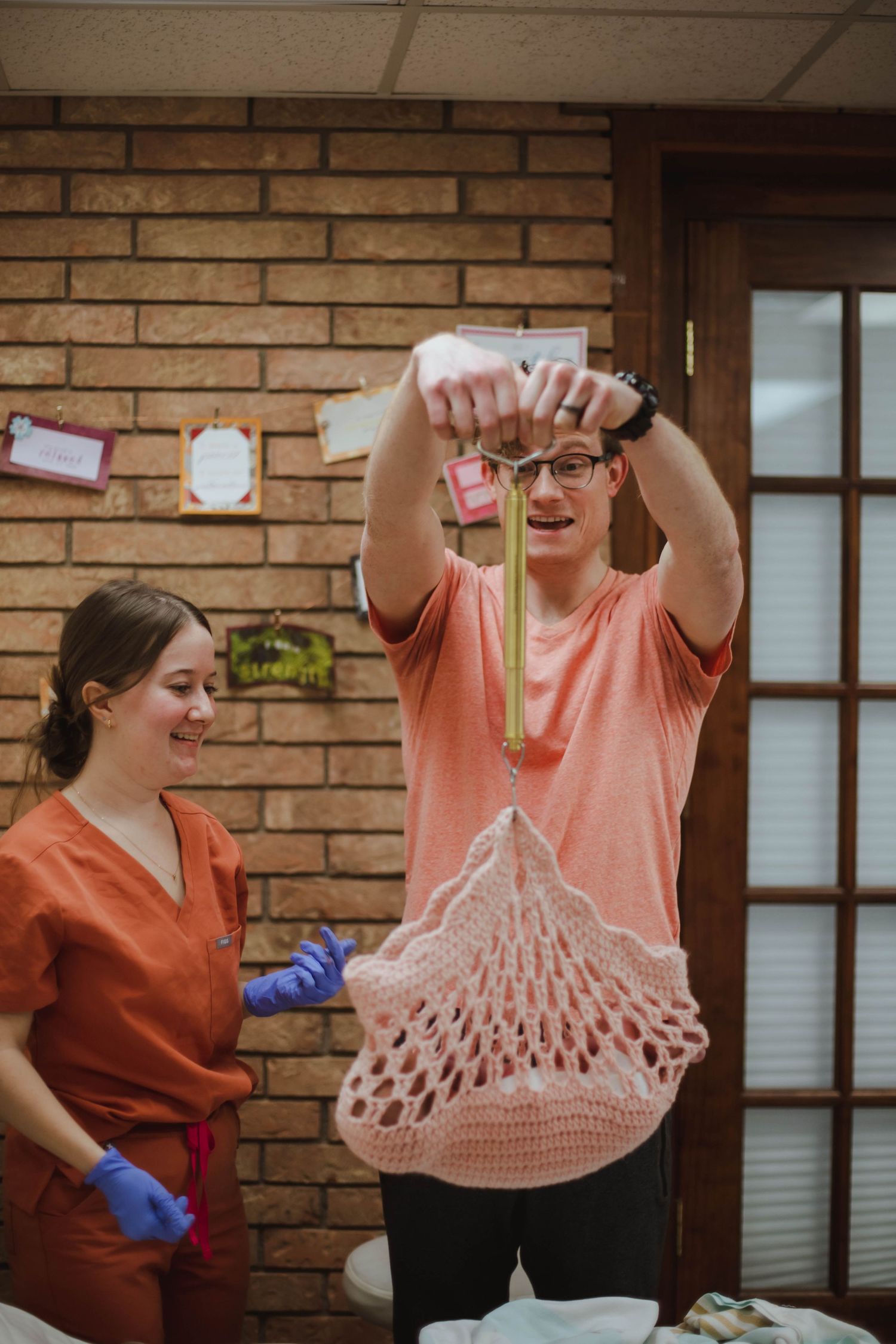 A nurse and father weigh a newborn baby using a hanging scale in a cozy home birth setting.