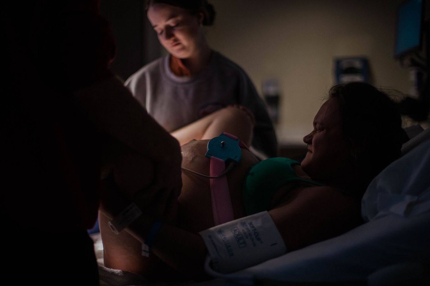 A medical professional assists a woman during labor in a dimly lit hospital room during childbirth.