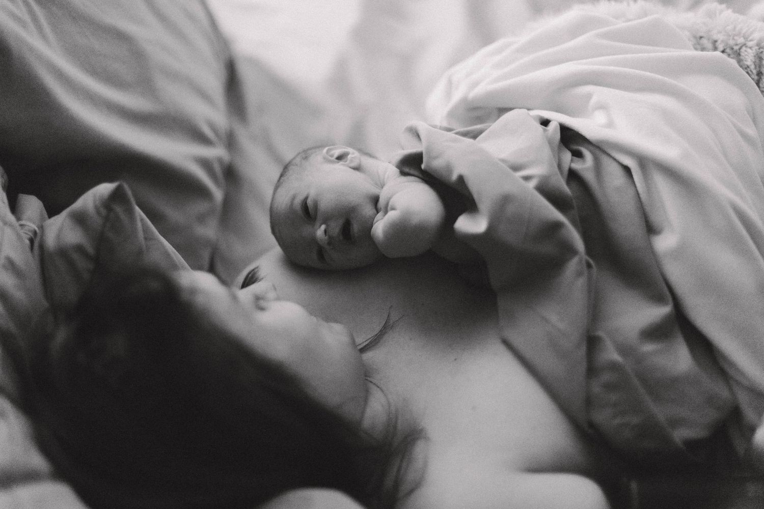 Black and white photo of a newborn baby lying on mother's chest shortly after birth.