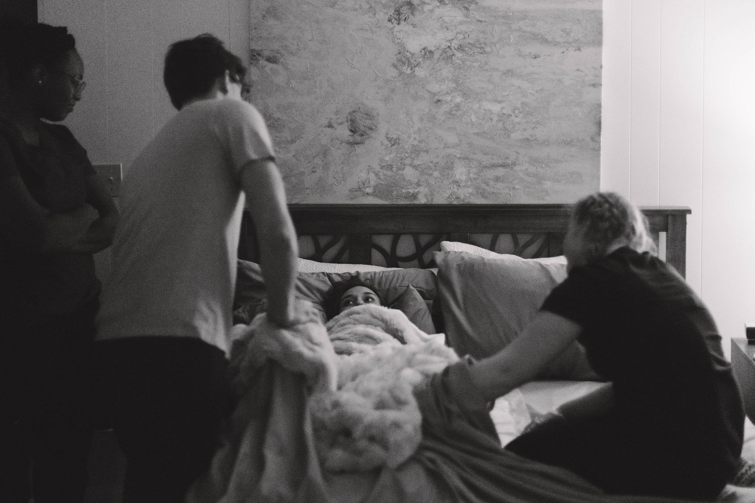 Black and white photo of home birth support team attending to laboring mother in bedroom.
