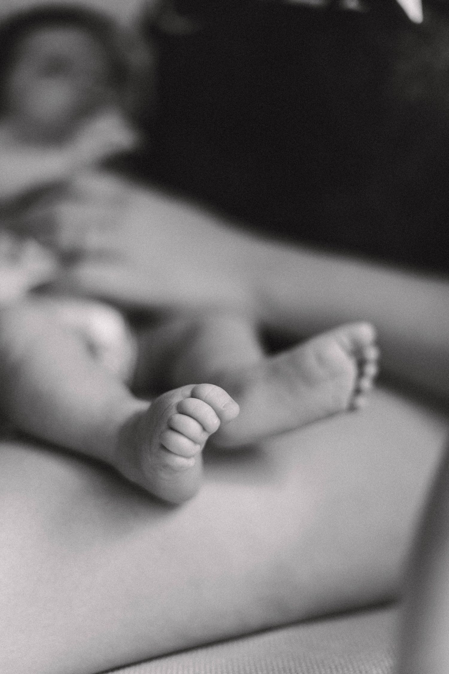 Close-up black and white photo of a newborns tiny feet resting on a soft surface.