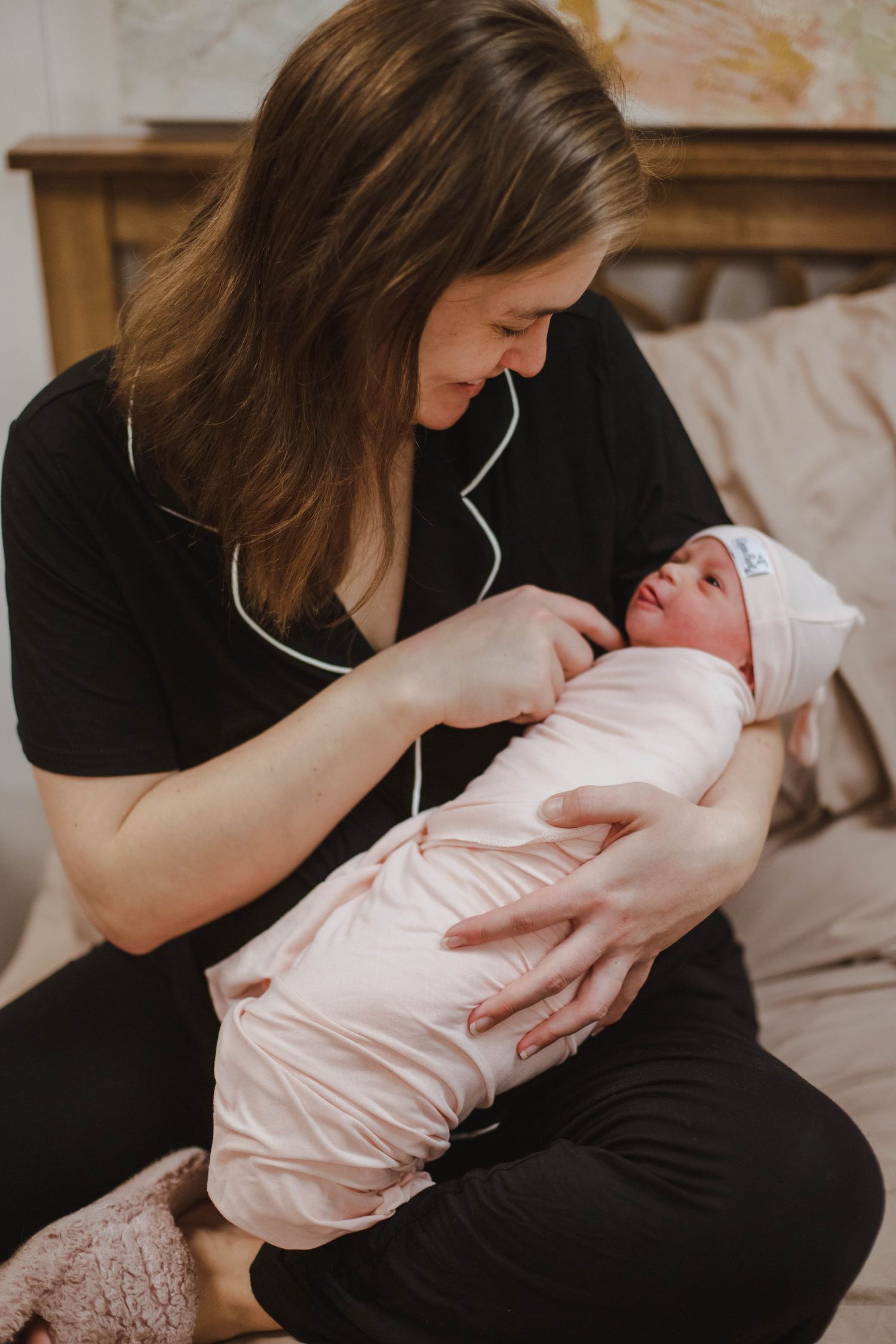 A new mother in black pajamas lovingly holds her swaddled newborn baby.