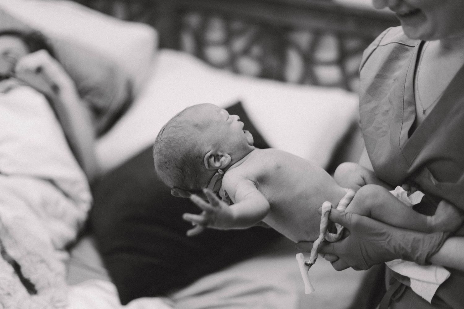 Black and white photo of midwife holding and examining a newborn baby after delivery.
