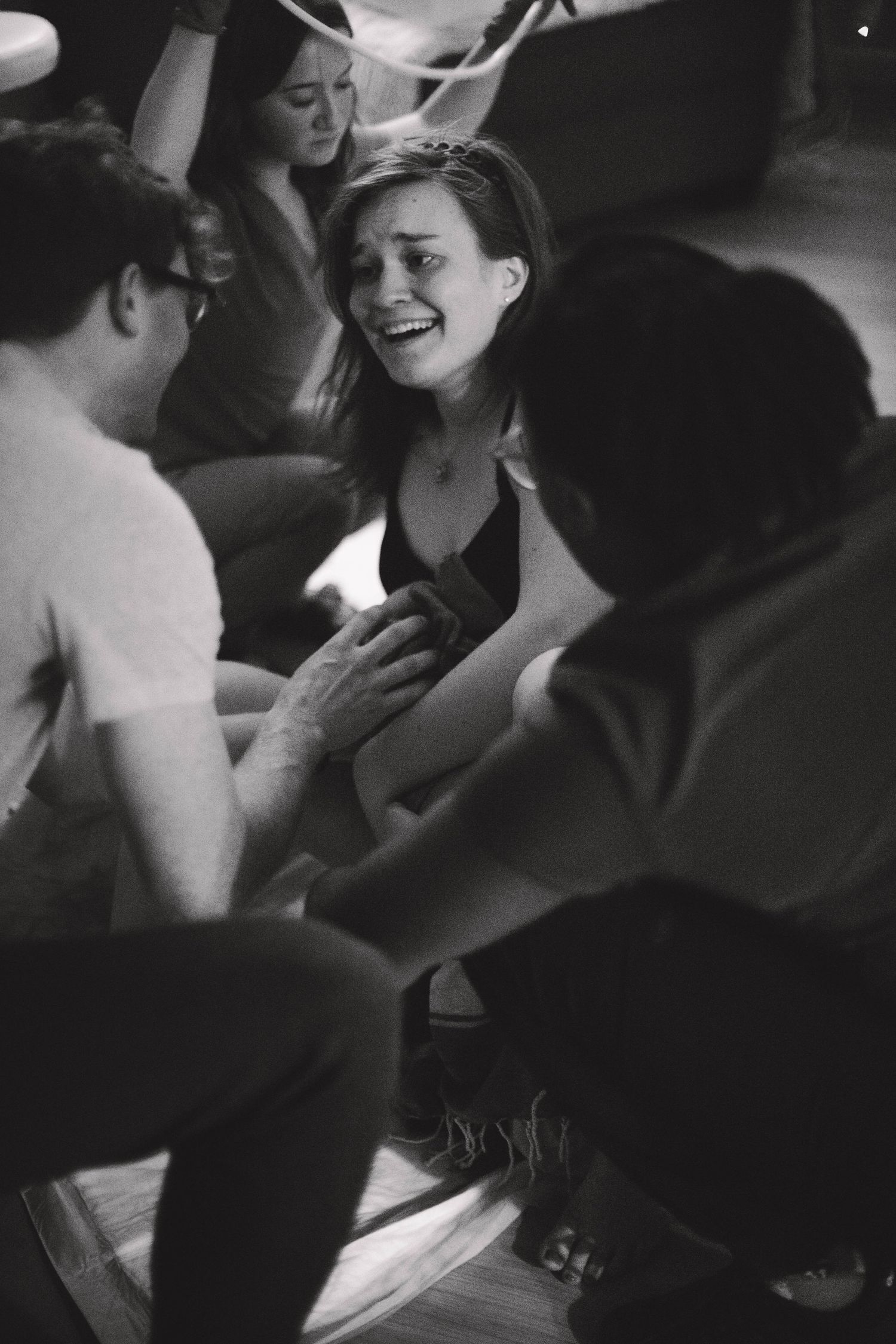 Black and white image of woman in active labor smiling through contractions surrounded by birth team.