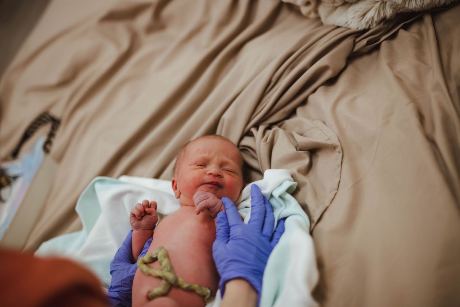 Newborn baby with umbilical cord being held by gloved hands moments after home birth delivery.