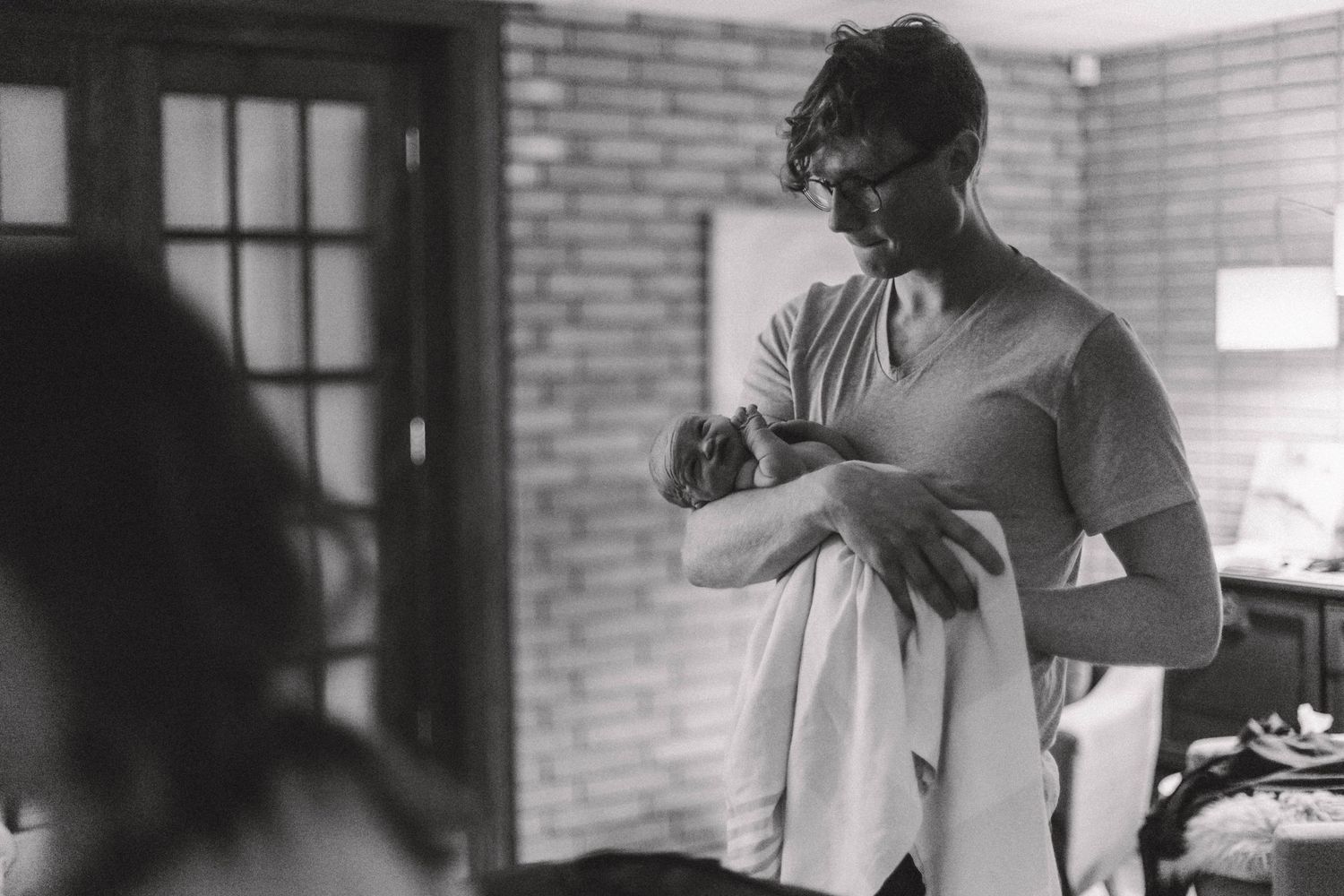 Black and white photo of a father carefully wrapping his newborn baby in a blanket after a home birth.