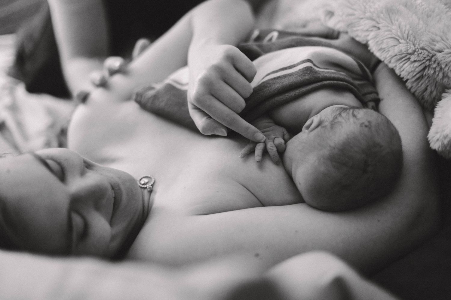 Black and white photo of smiling mother holding newborn baby on her chest after birth.