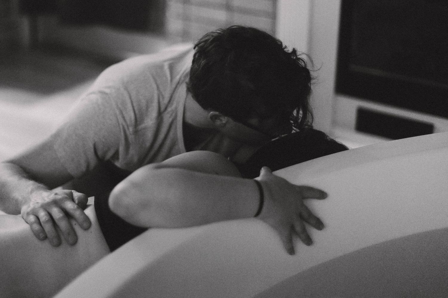 Black and white photo of man supporting laboring woman leaning over birth tub.