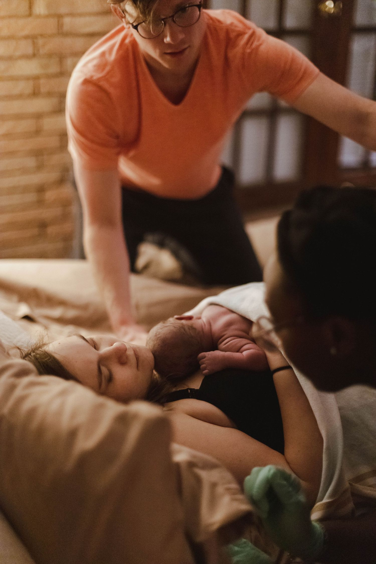 A midwife assists a mother lying in bed as she holds her newborn baby during a home birth.