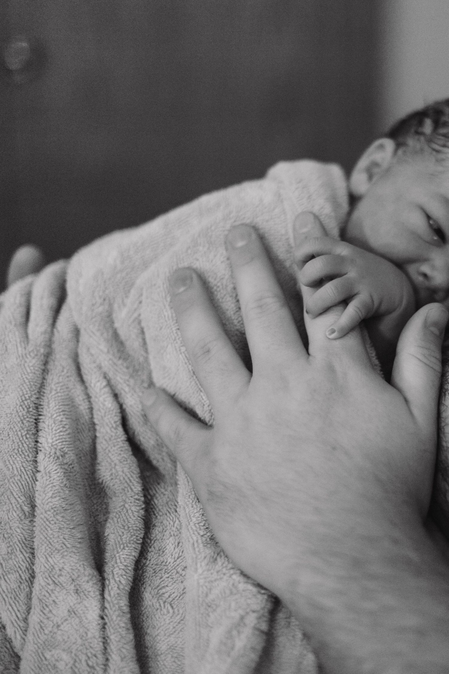 Black and white close-up of newborn baby wrapped in towel held by parent.