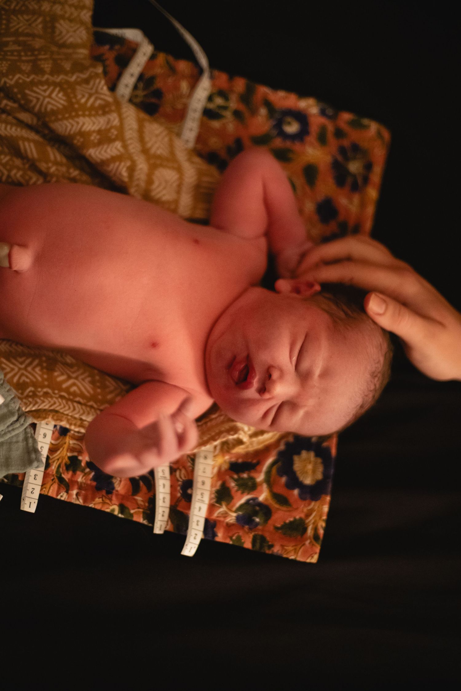 Newborn baby lying on patterned blanket with hospital identification tags attached.