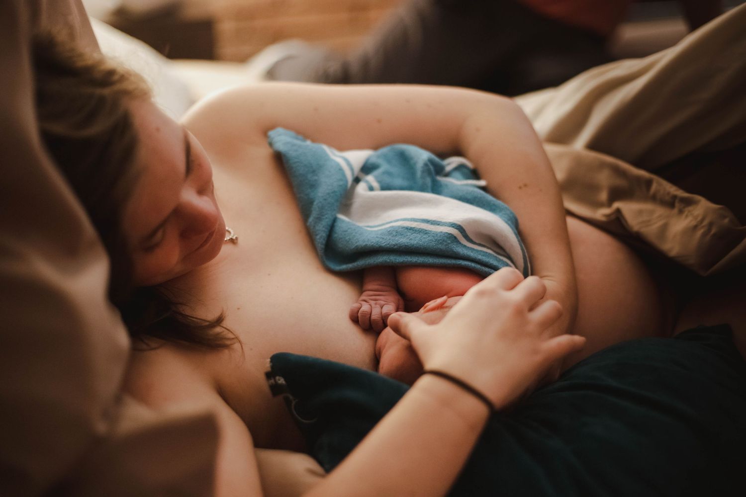 New mother breastfeeding her newborn baby while lying down after home birth.