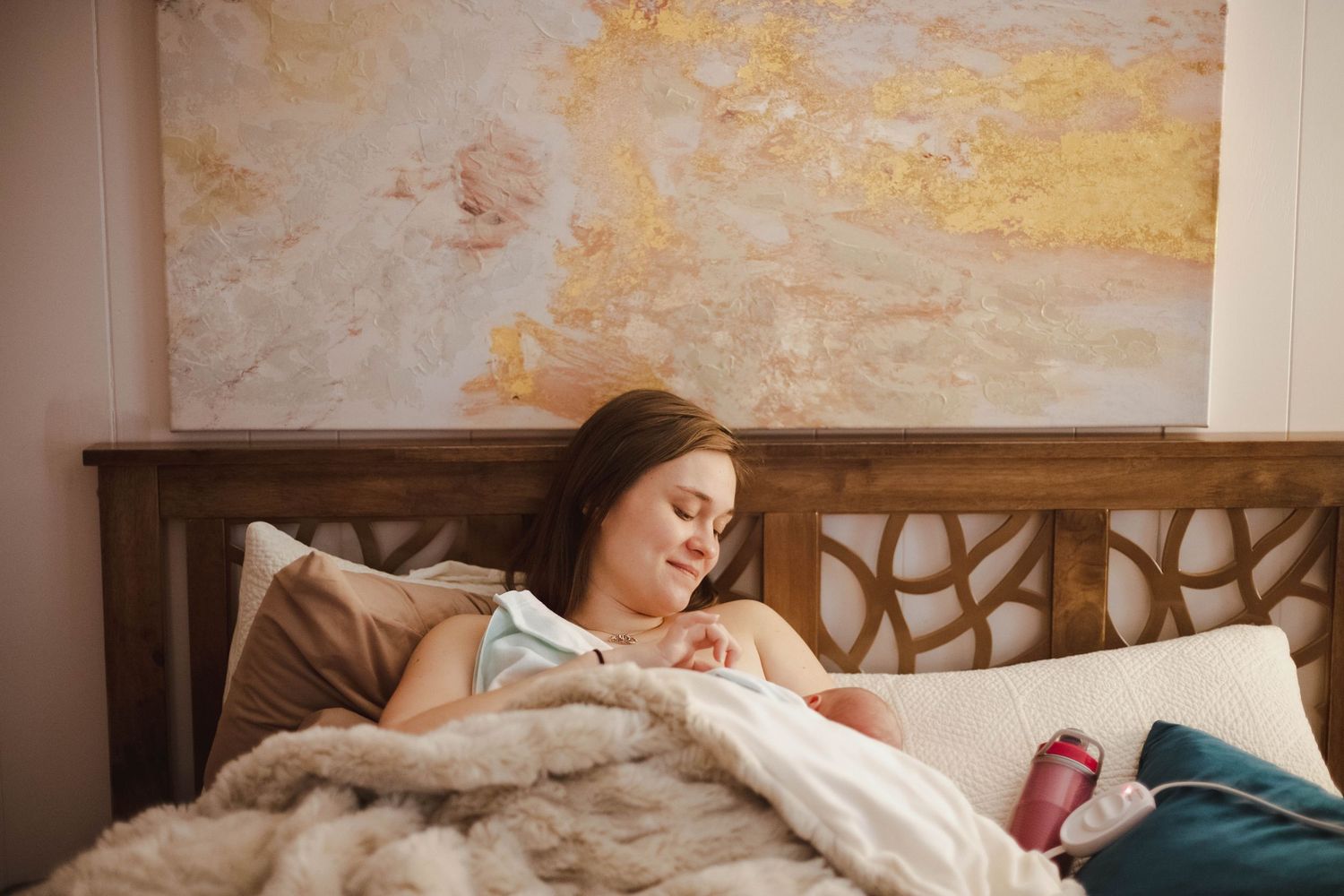 A new mother smiles while cradling her newborn baby in a warm, cozy bedroom.