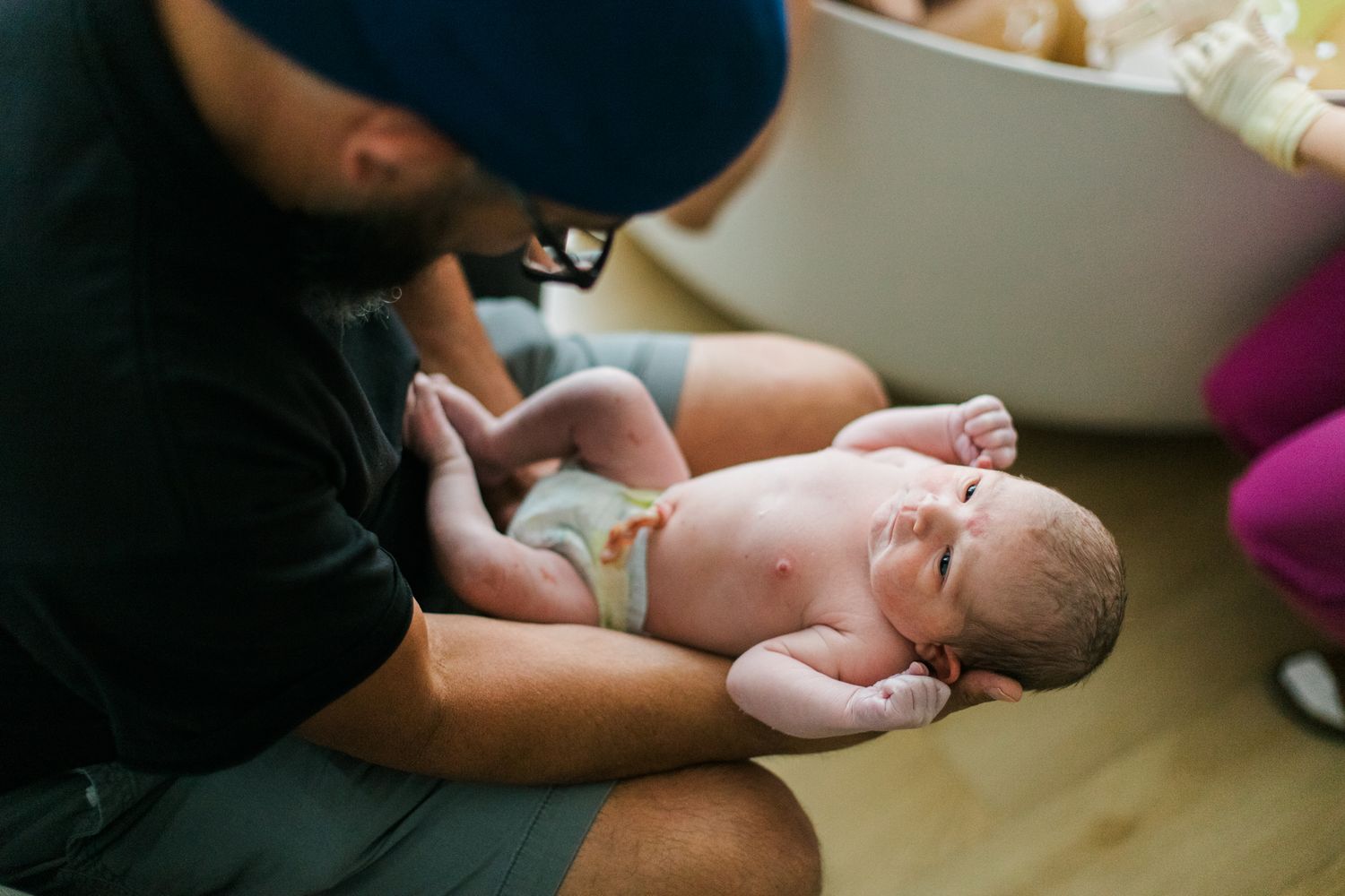 A father tenderly holds his newborn baby on his lap shortly after birth in a hospital room.