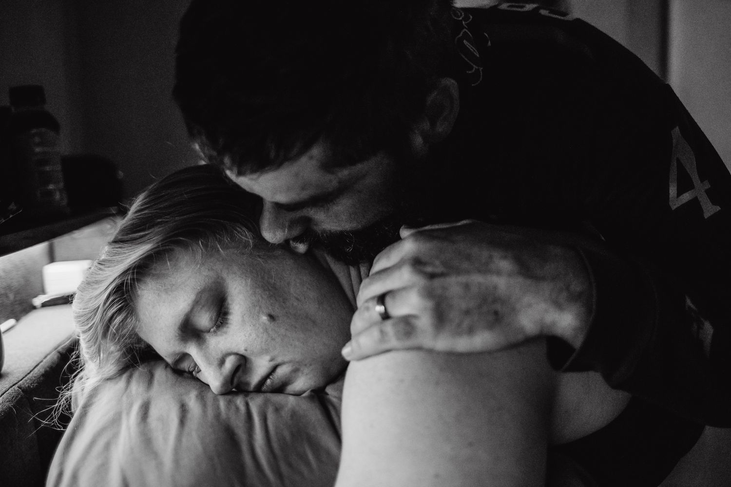 Black and white photo of a man tenderly embracing and kissing a mother in labor.