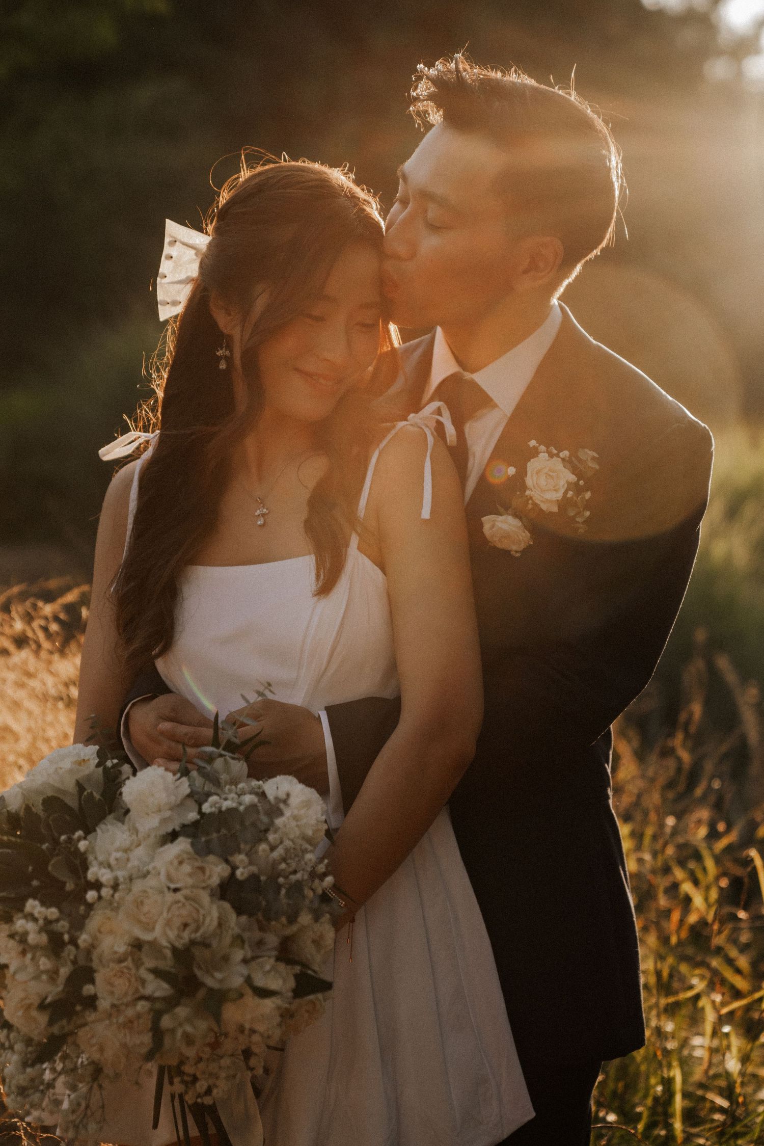 A couple shares intimate moments in a golden sunset field with a white bridal bouquet.