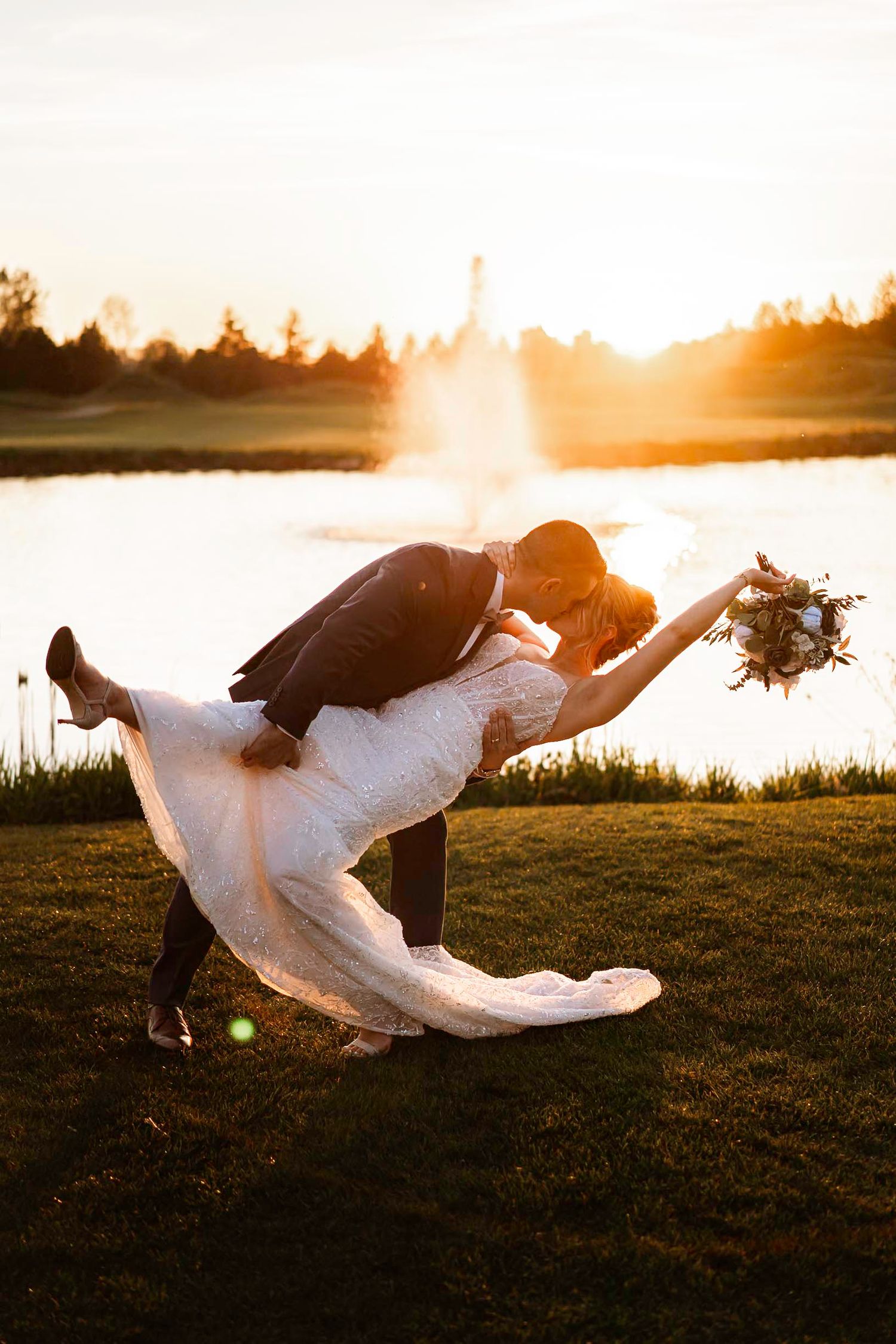 Dramatic sunset silhouette of couple embracing on grassy lakeside.