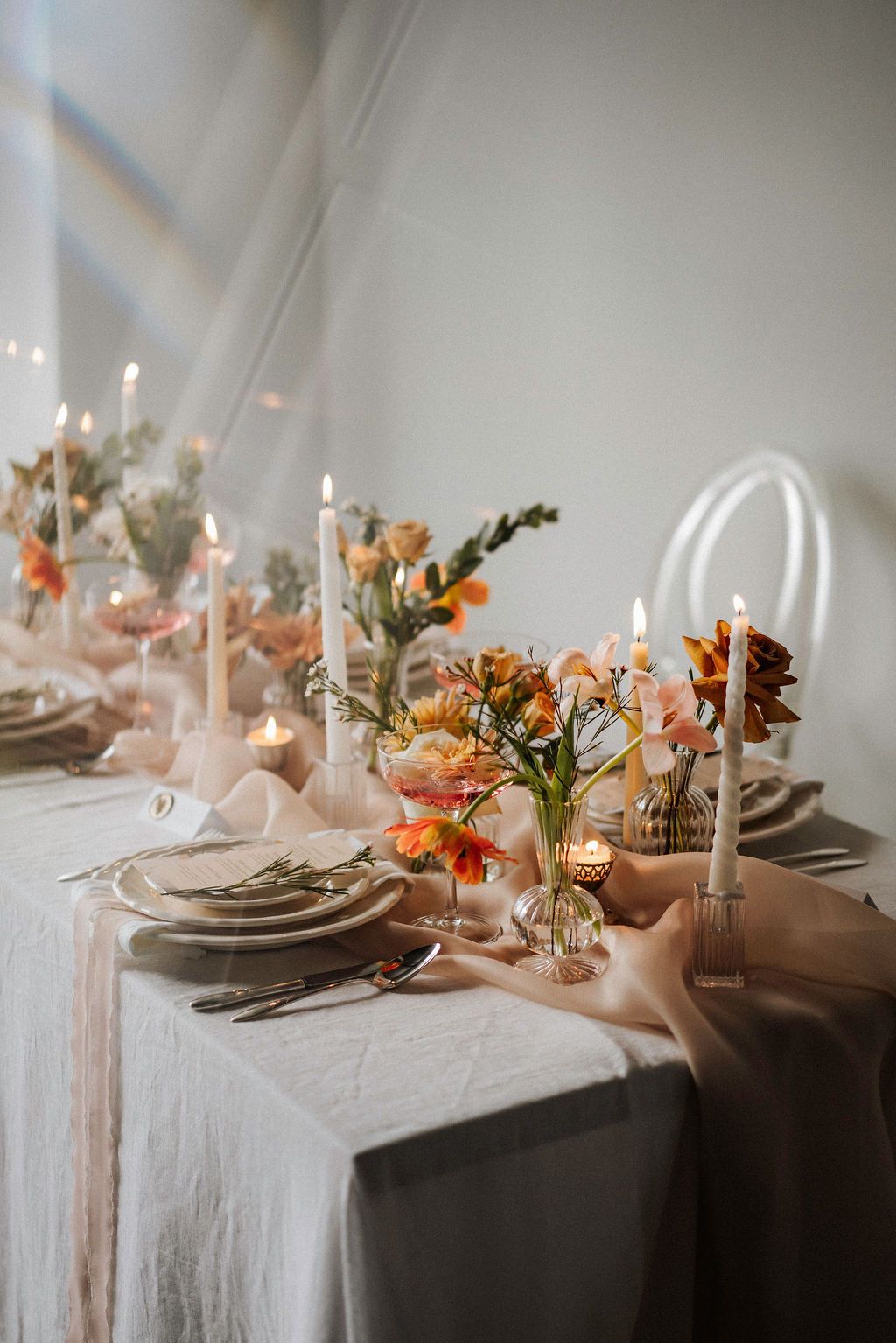 Elegant table setting with candles, peach florals, and neutral linens.