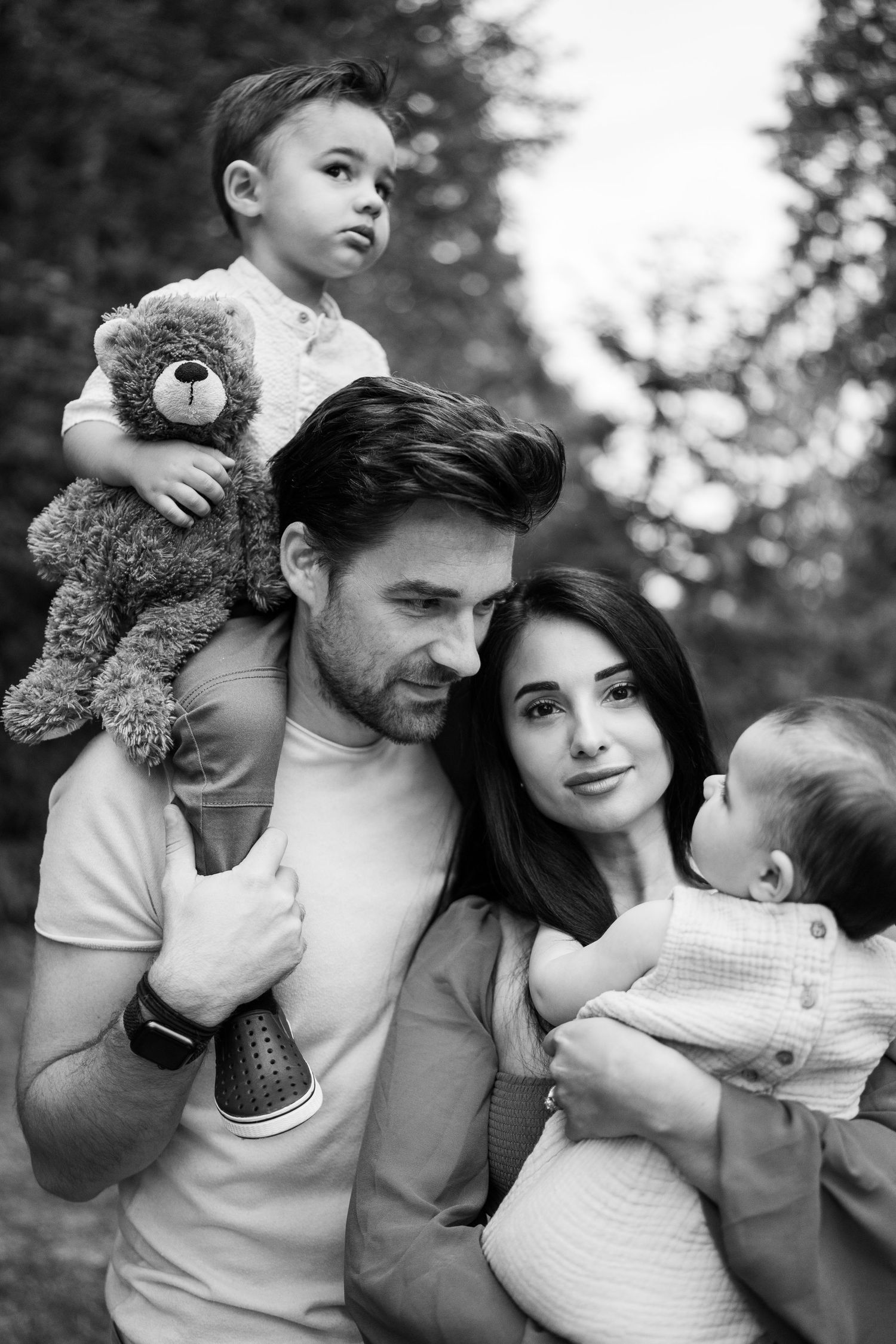 Family portrait in black and white with child holding teddy bear.