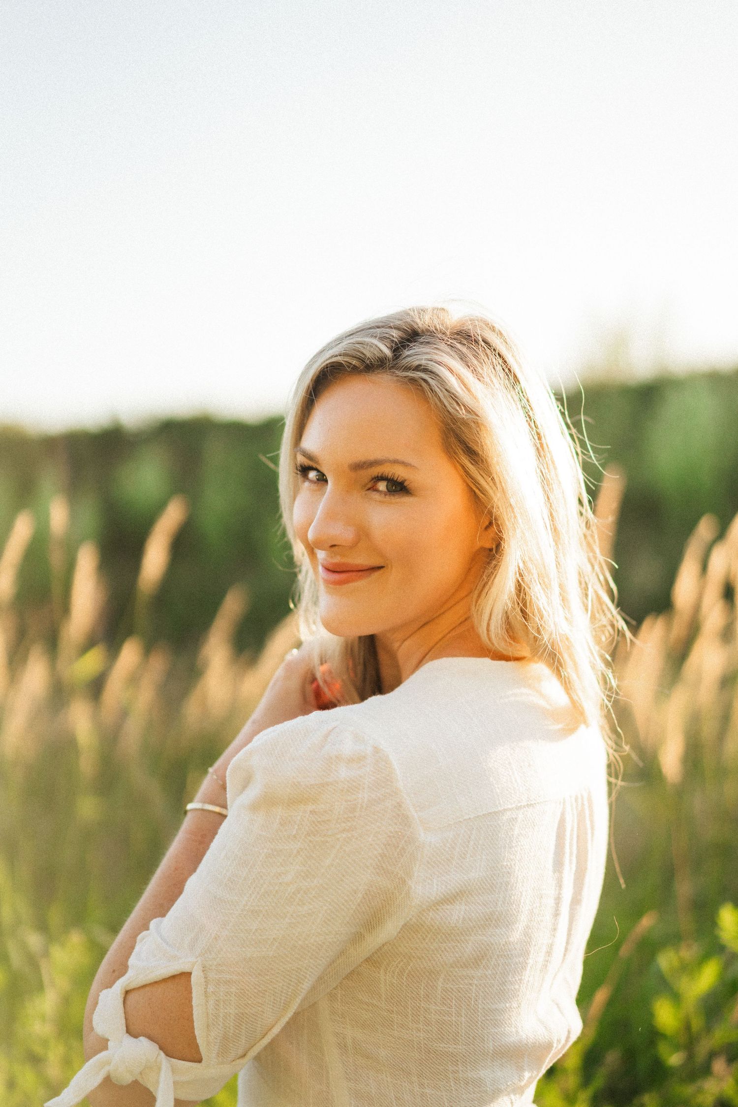 Backlit portrait in white dress against field of tall grass.