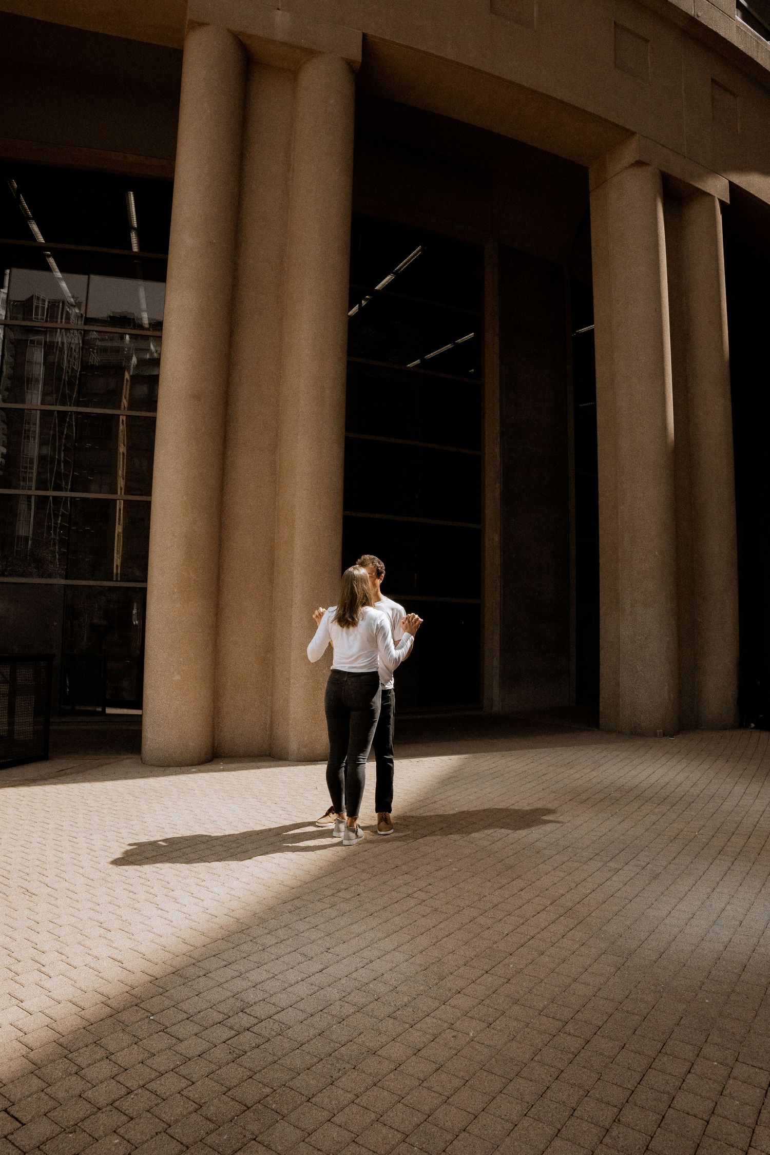 Couple walking through dramatic sunlit colonnade with geometric shadows.