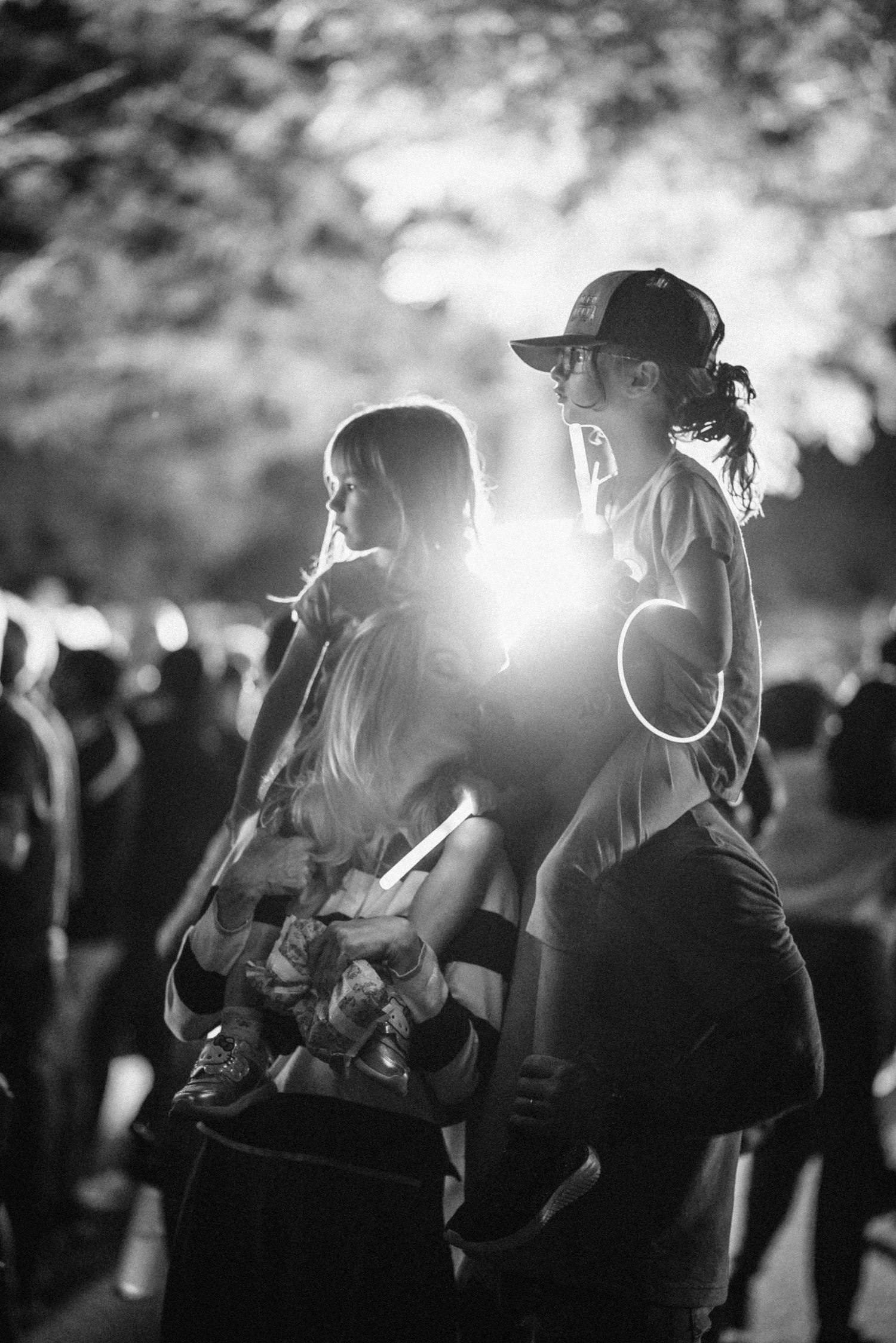 Black and white silhouette of two people standing in a crowd with sun flare creating dramatic backlighting.