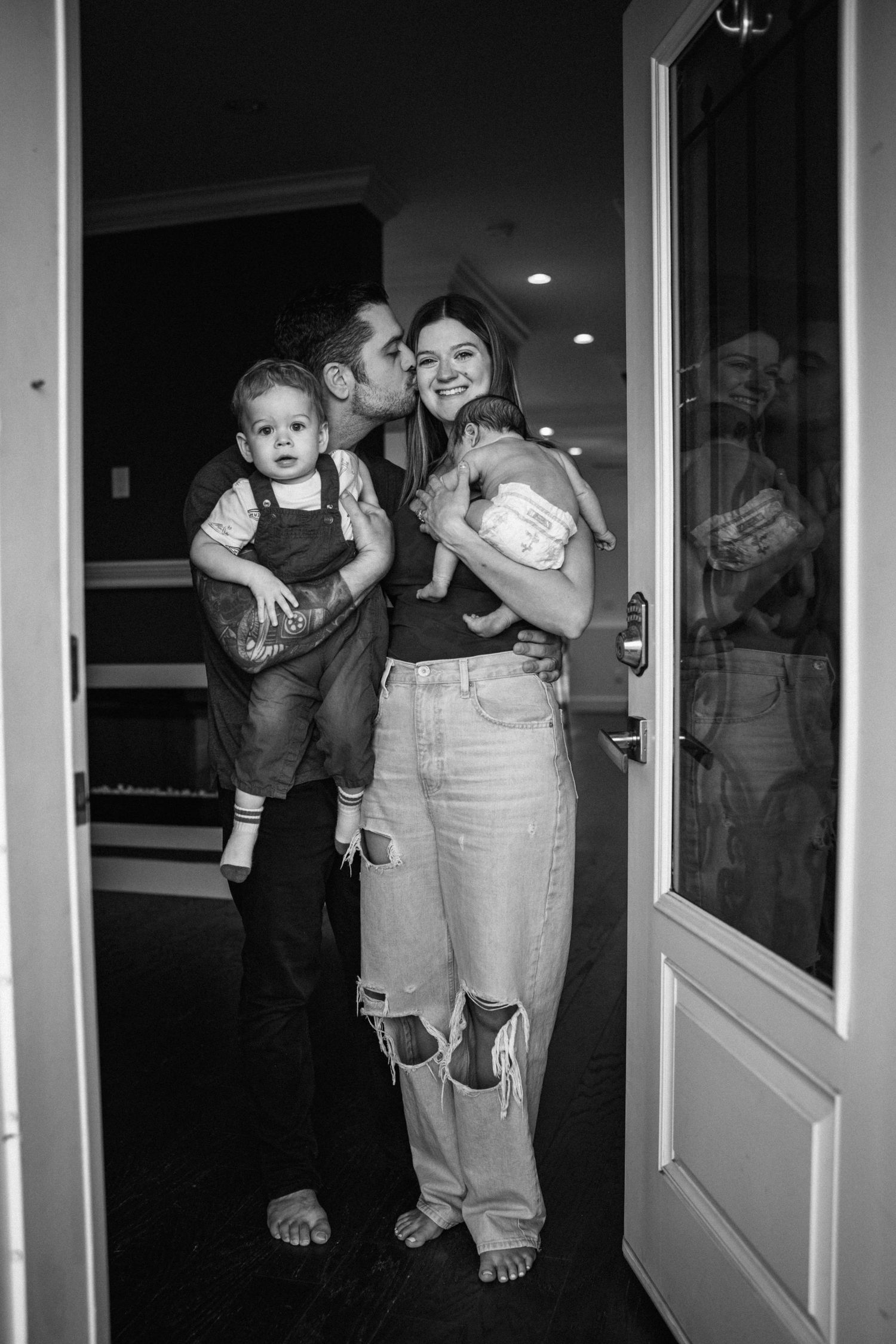 A black and white candid family moment showing affection while standing in a doorway.