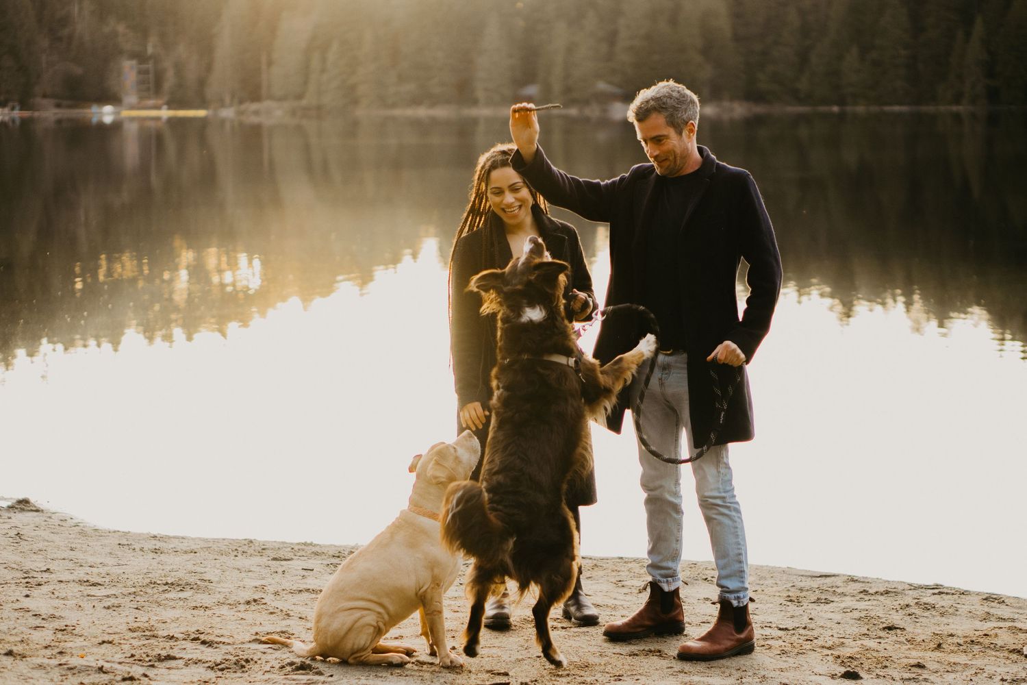 A couple with two dogs enjoying sunset by a serene lake.