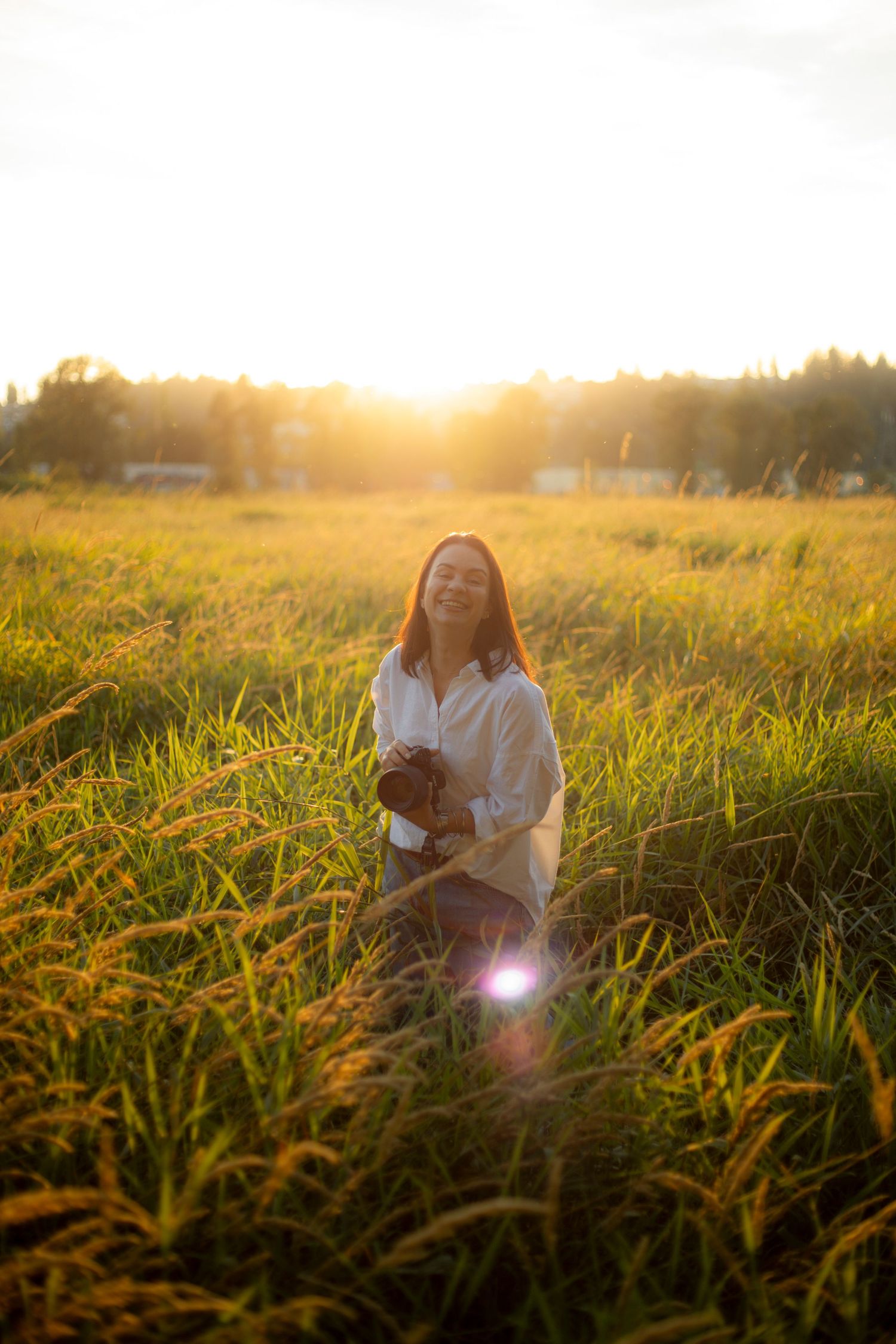 A photographer sits in tall grass during golden hour sunset.