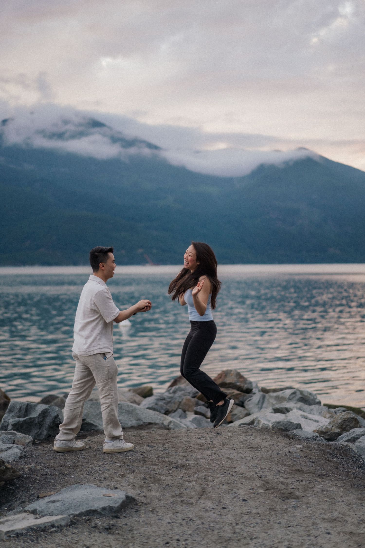A romantic proposal scene unfolds on rocky shore with mountains and lake in the background.