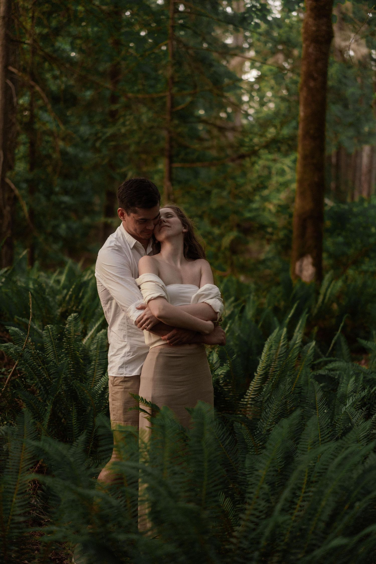 Intimate couples photoshoot among tall trees and ferns in a forest setting.