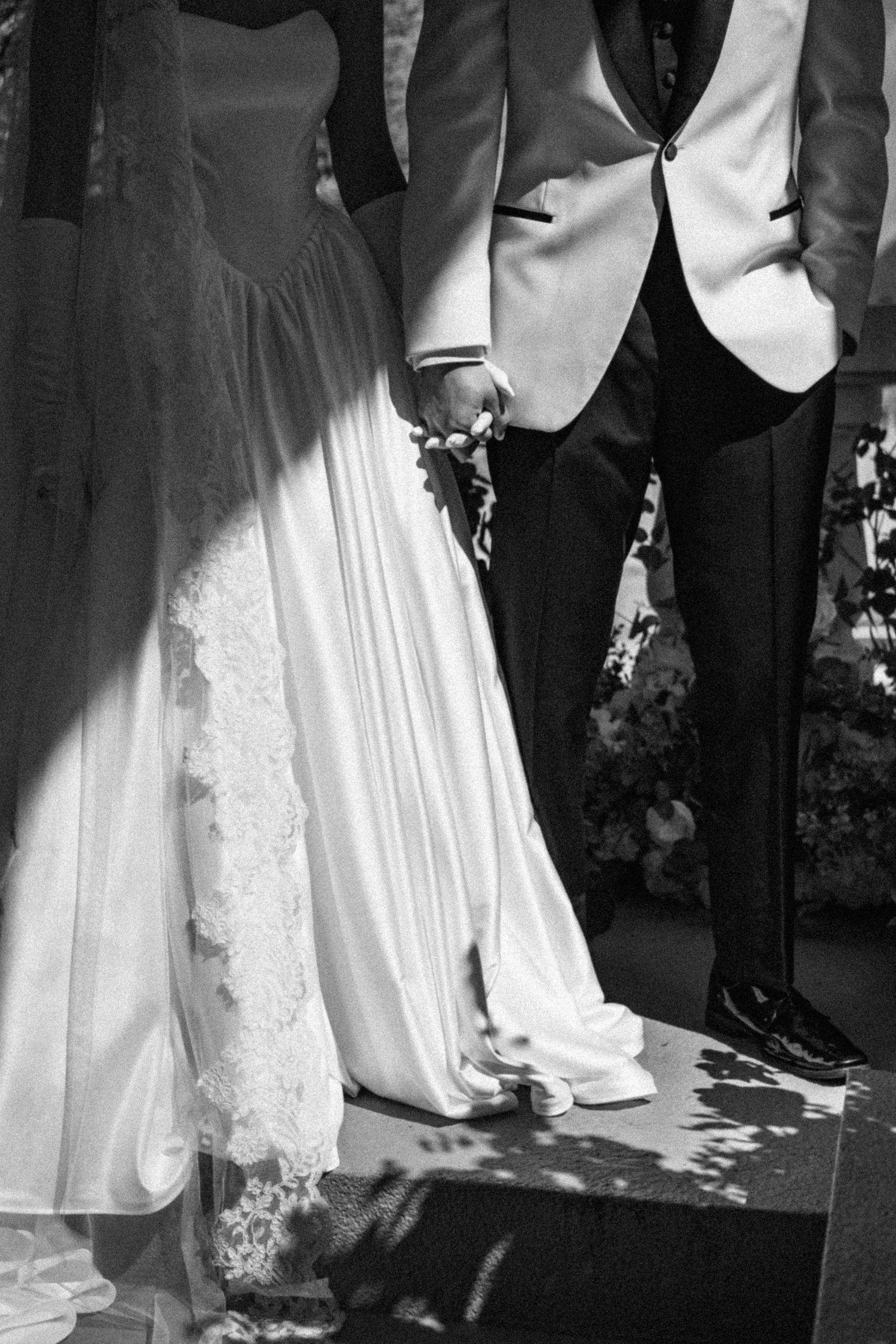 Black and white photo showing formal wedding attire with flowing white dress and dark suits.