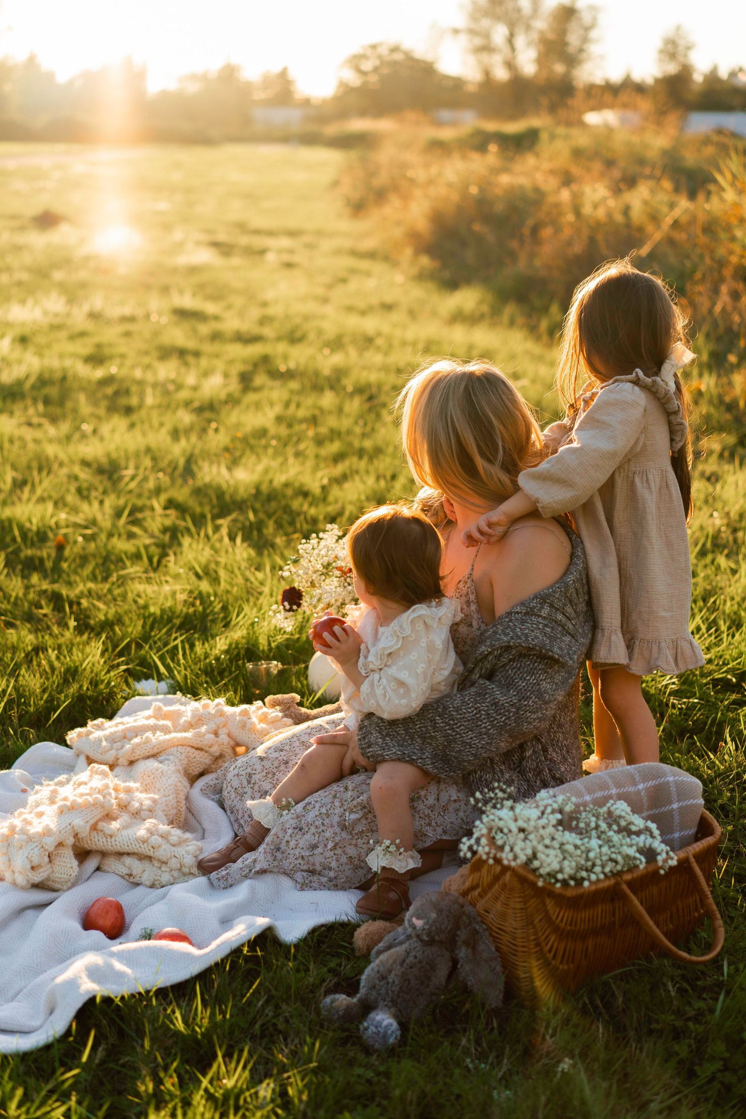 Family sits on picnic blanket in golden meadow during sunset.