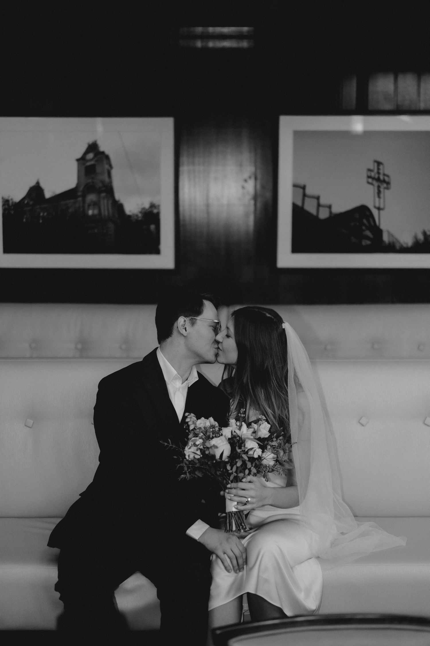 Newlyweds sharing romantic moments on a white couch against a wall of black and white artwork.