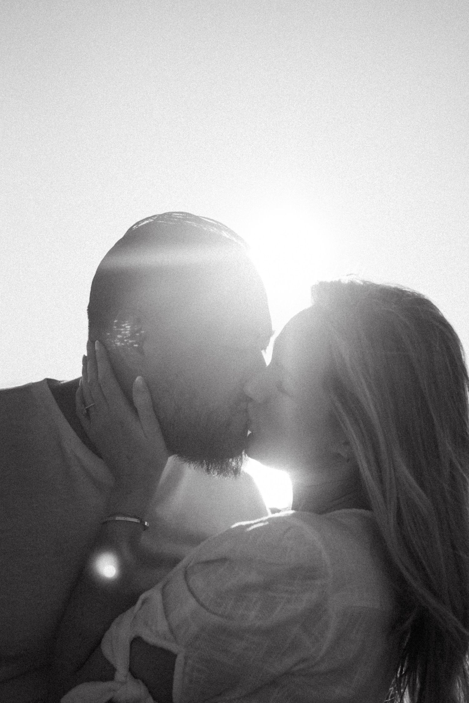 Silhouettes of a couple sharing an intimate moment against bright sunlight.