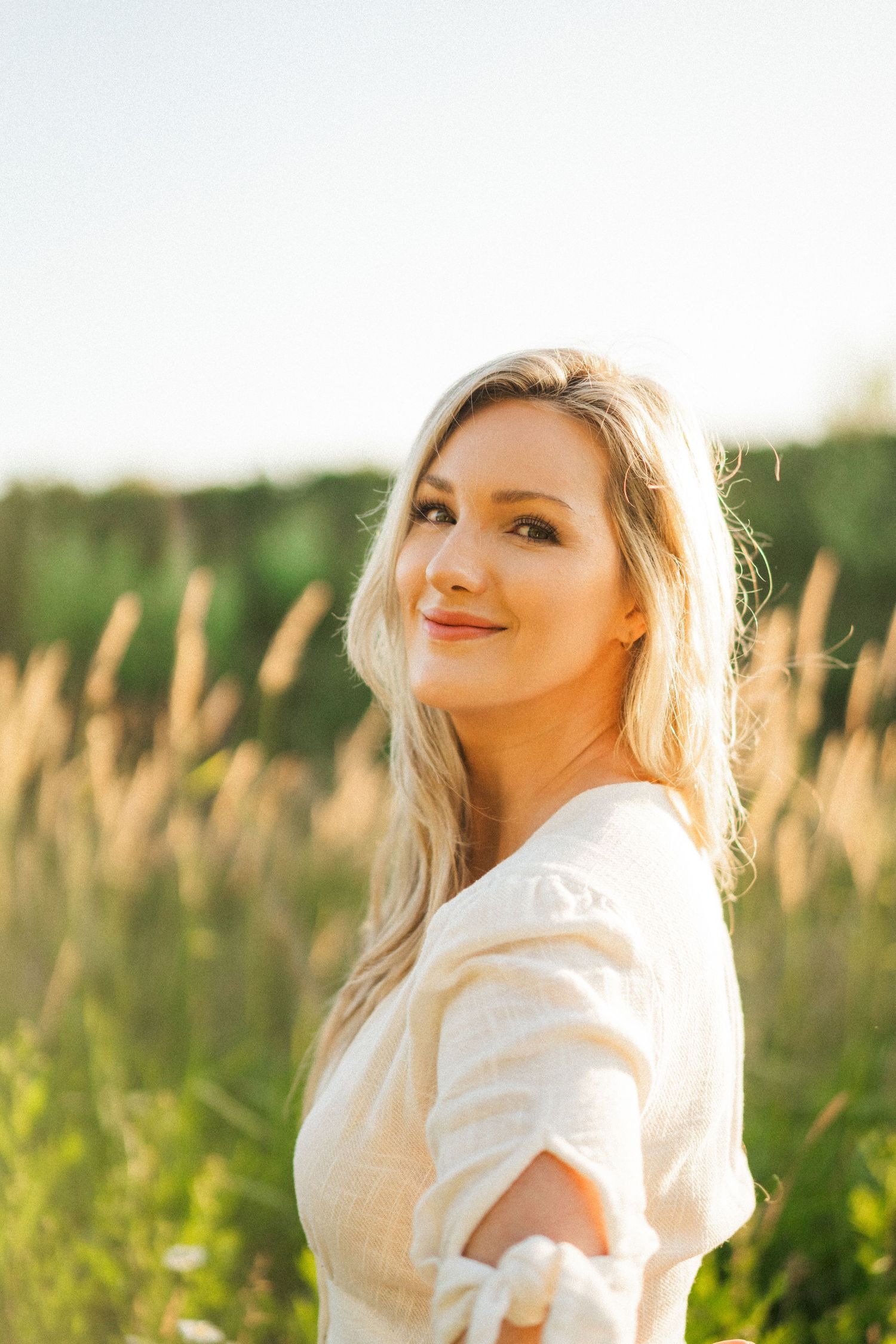 A person in white poses in a sunlit field of tall grass during golden hour.