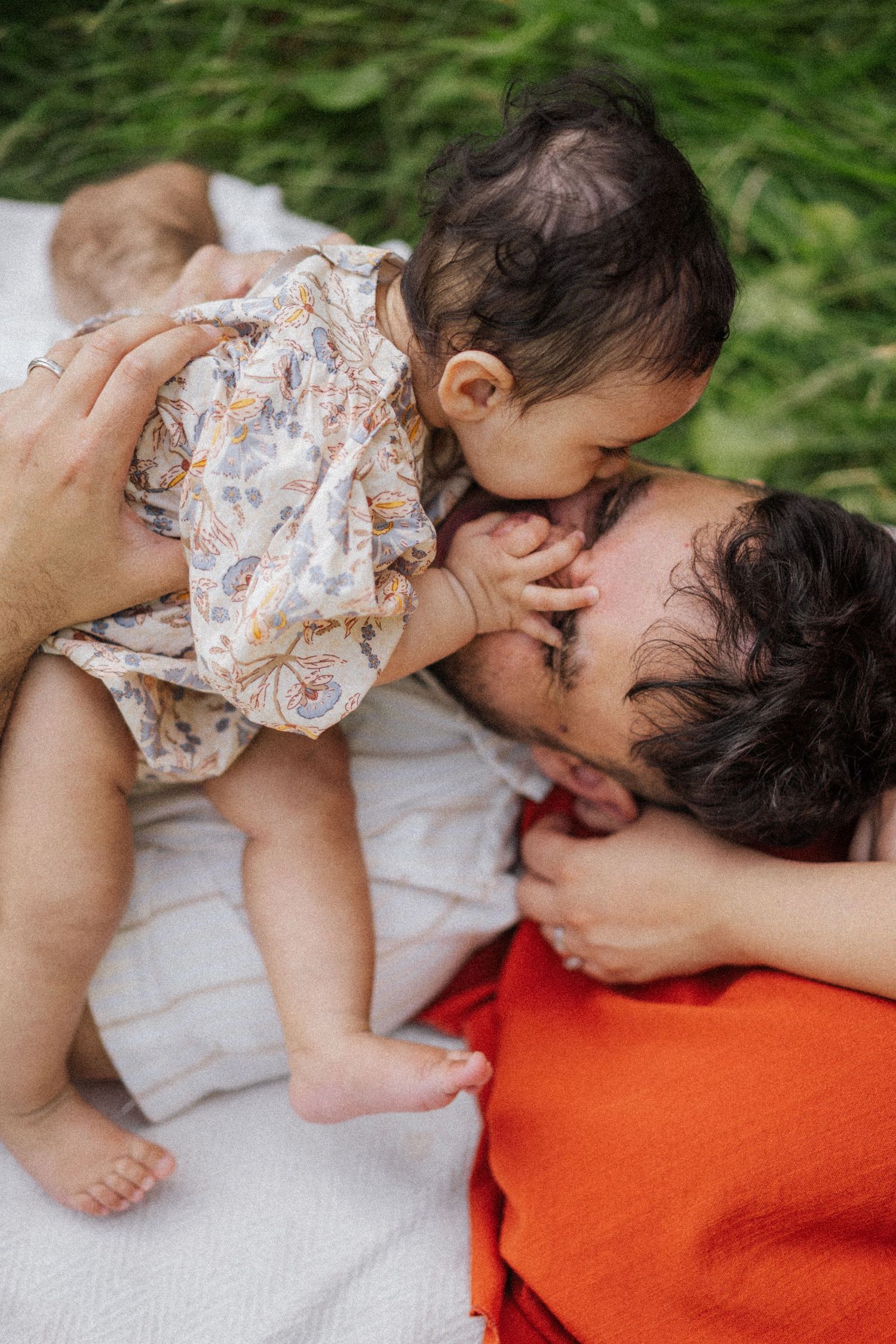 Tender moment shared between parent and baby on a white blanket outdoors.