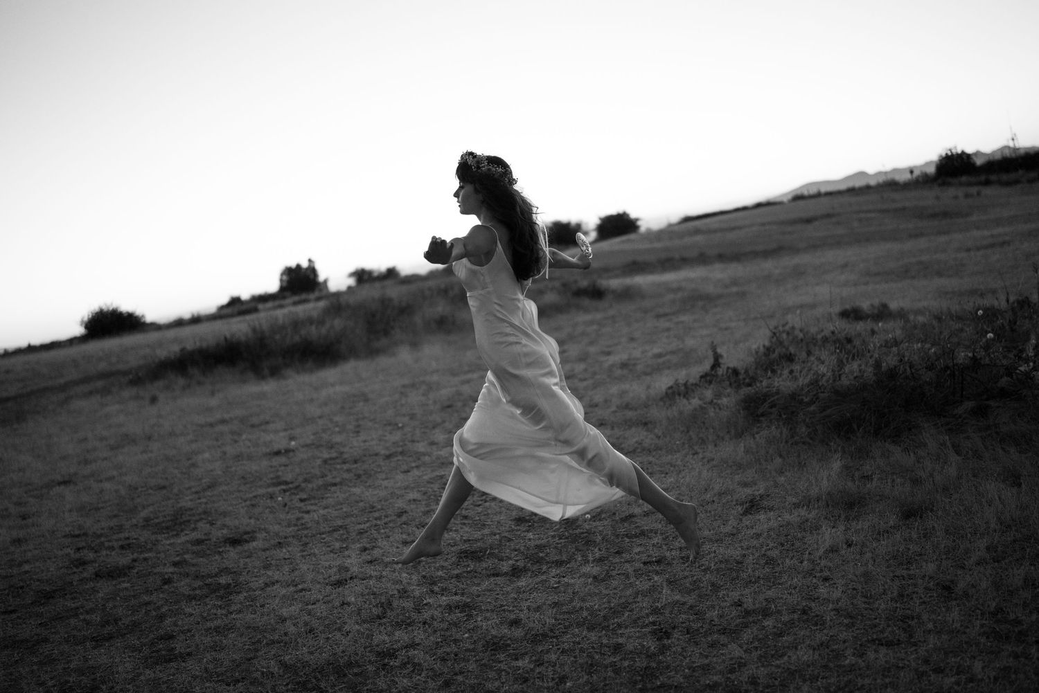 Silhouette of person running freely across a grassy hilltop at dusk.