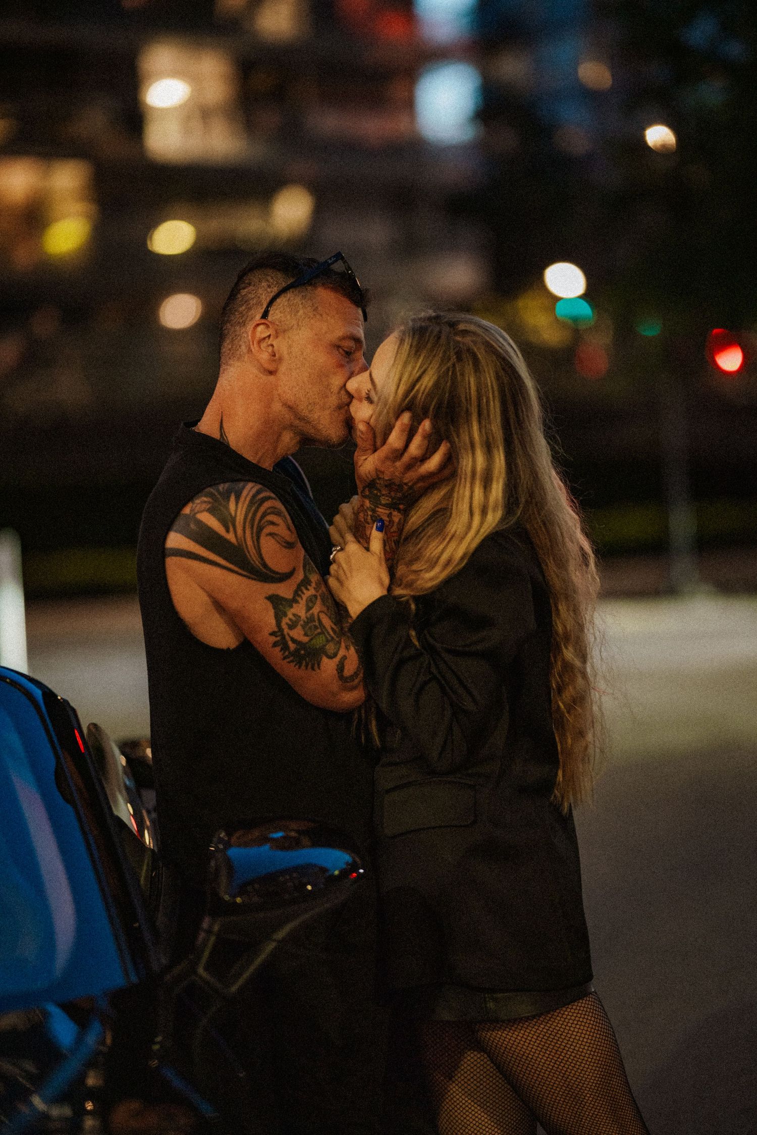 A couple shares an intimate kiss at night in a dimly lit urban setting.