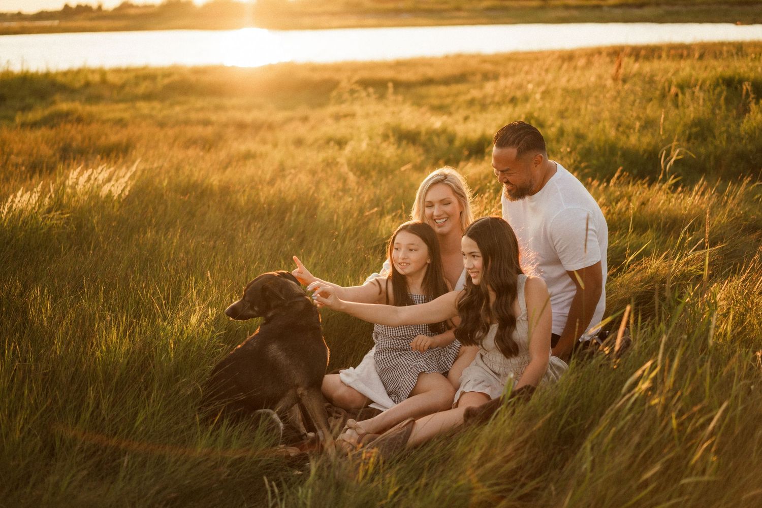 Family relaxing together in tall grass during golden hour sunset.