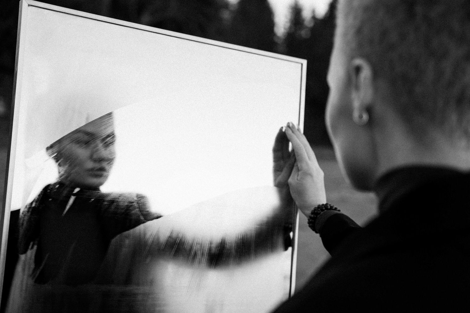 A blurry black and white reflection in a mirror shows a figure with a raised hand creating a dramatic silhouette effect.