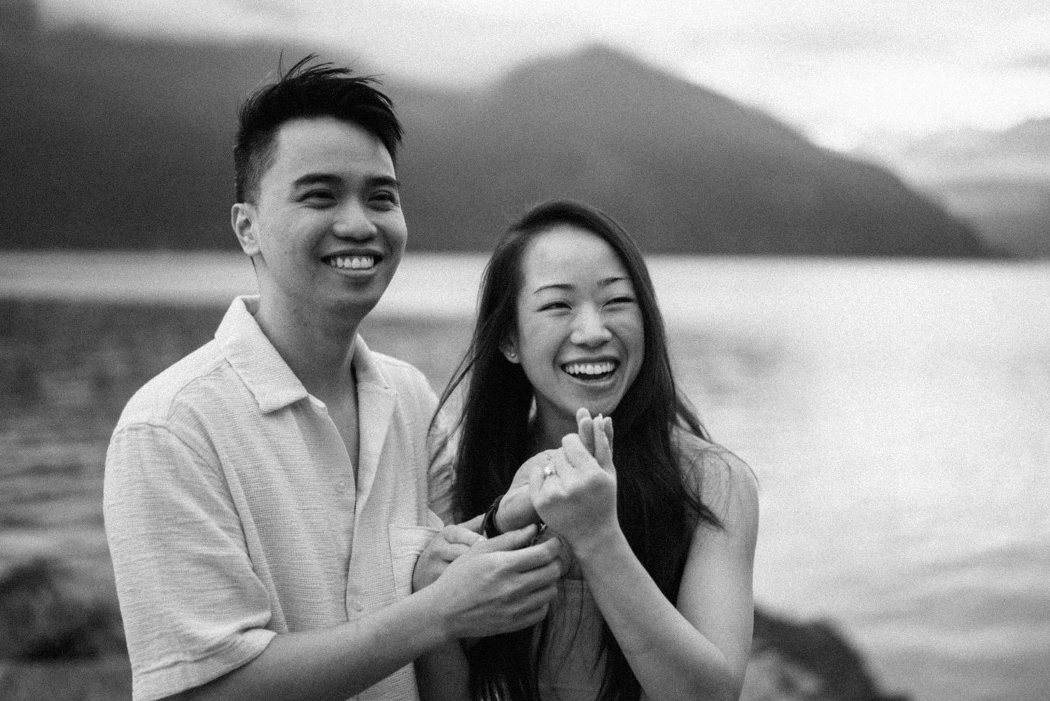 A couple shares a joyful moment against a scenic mountainous backdrop near a lake.