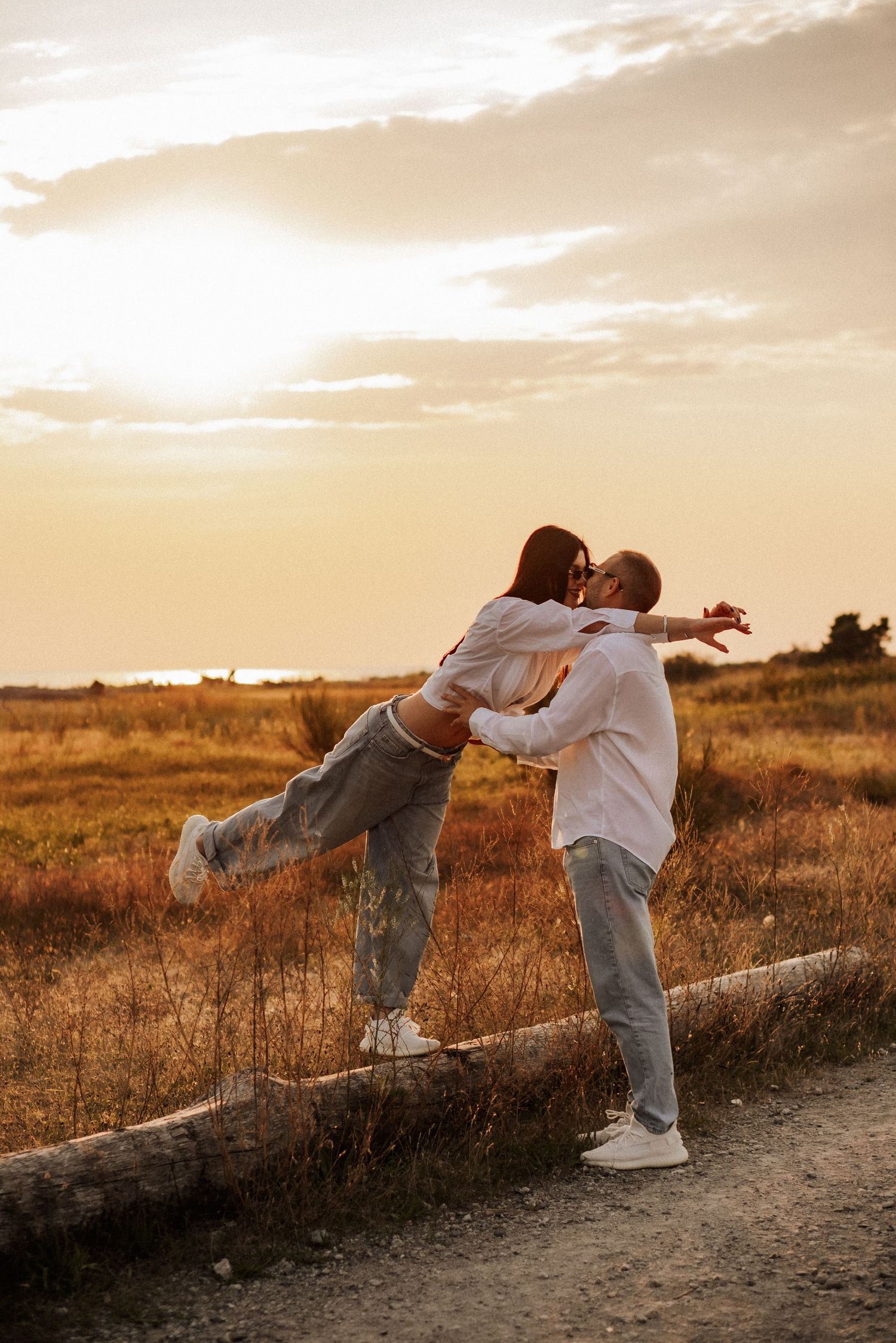 Two people playfully interact on a dirt path at sunset with golden light illuminating the autumn landscape.