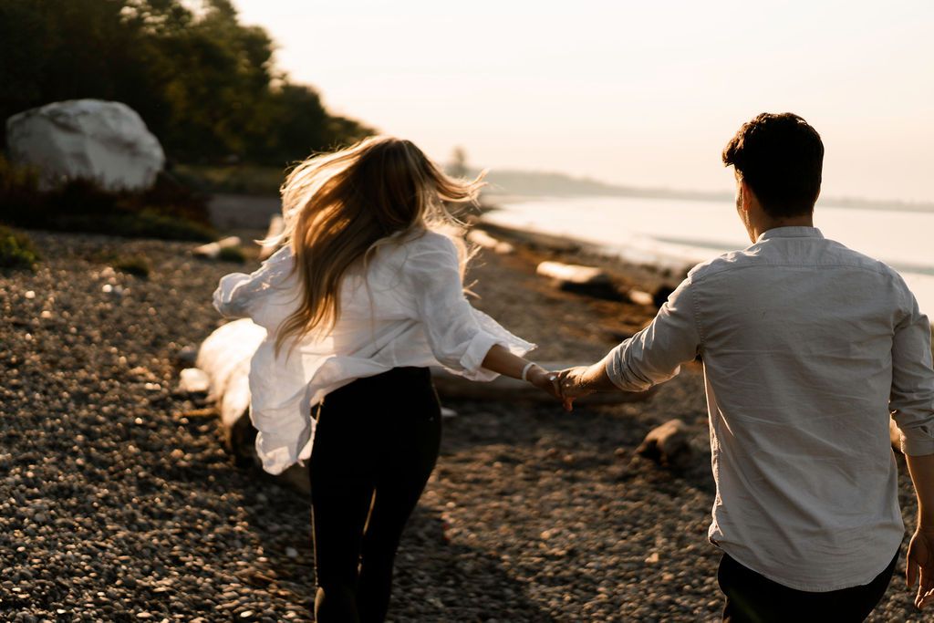 Couple walking and playing along rocky beach at sunset.