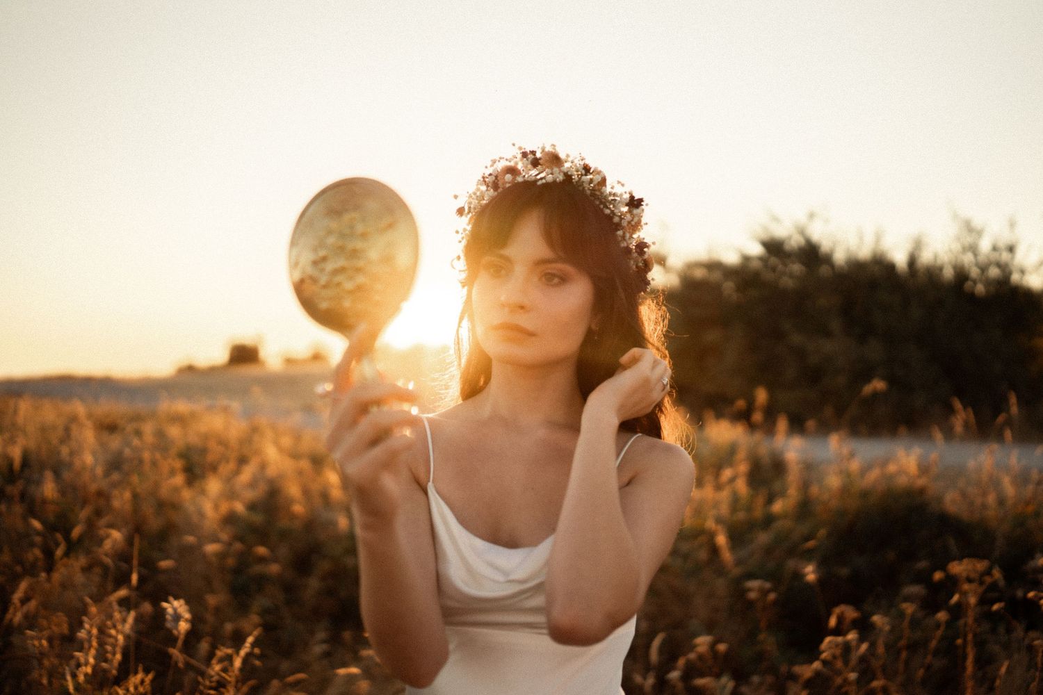 Ethereal sunset portrait features a woman in white holding a reflective sphere in a golden field.