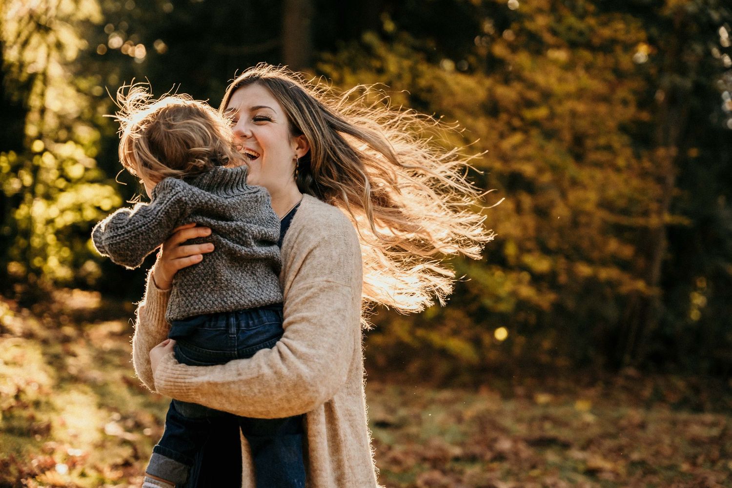 A couple embraces in a romantic autumn forest setting with golden sunlight filtering through the trees.