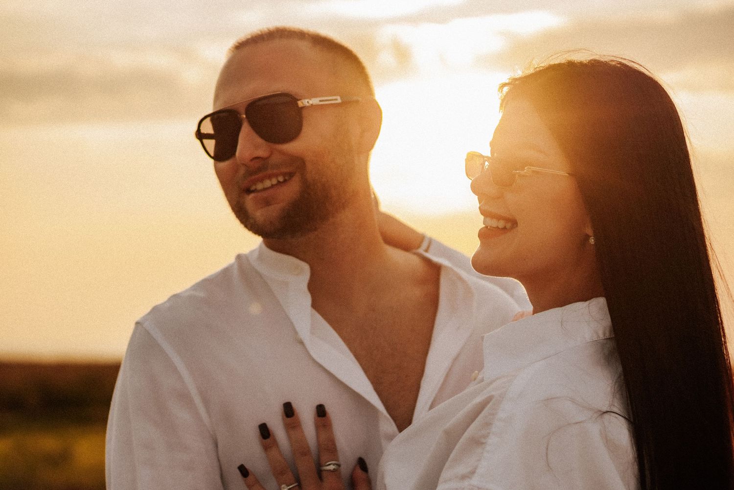 A romantic couple shares tender moments in golden sunlight while wearing white clothing and sunglasses.
