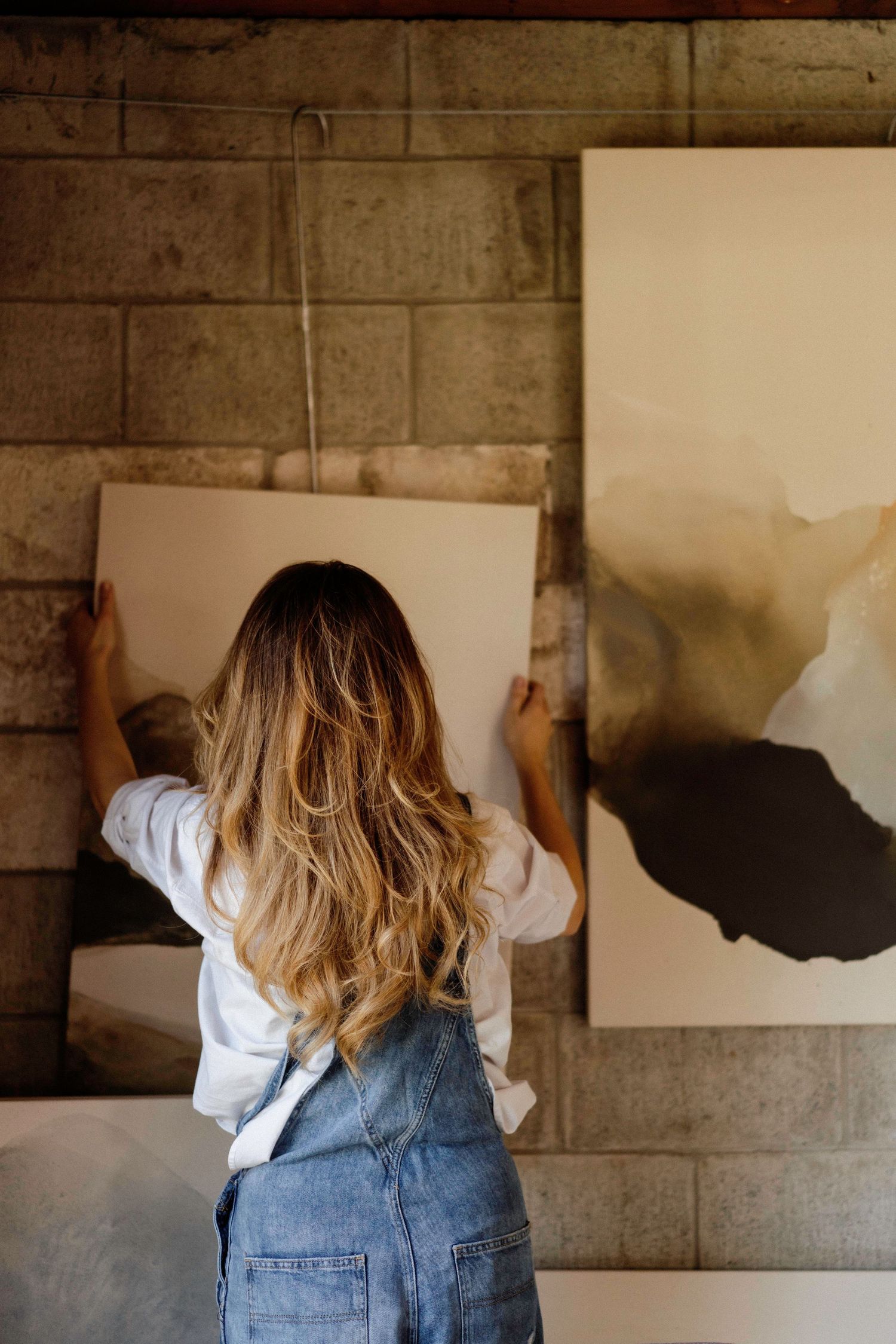 Artist painting on white canvas mounted on industrial concrete wall.